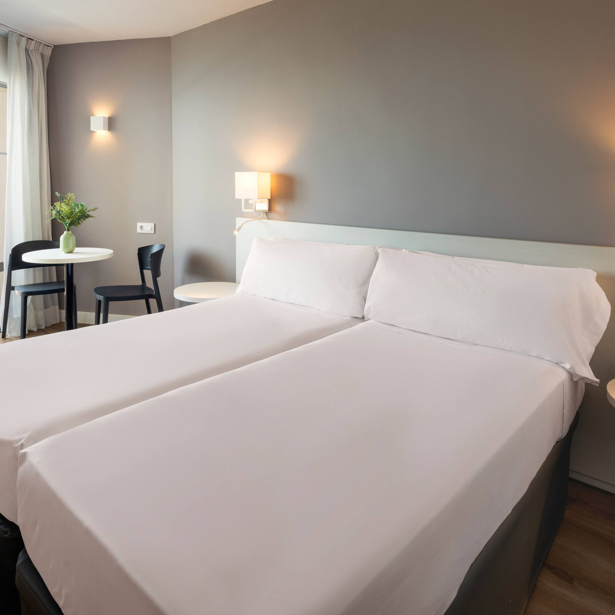 a bed with white sheets and a table with chairs and a lamp