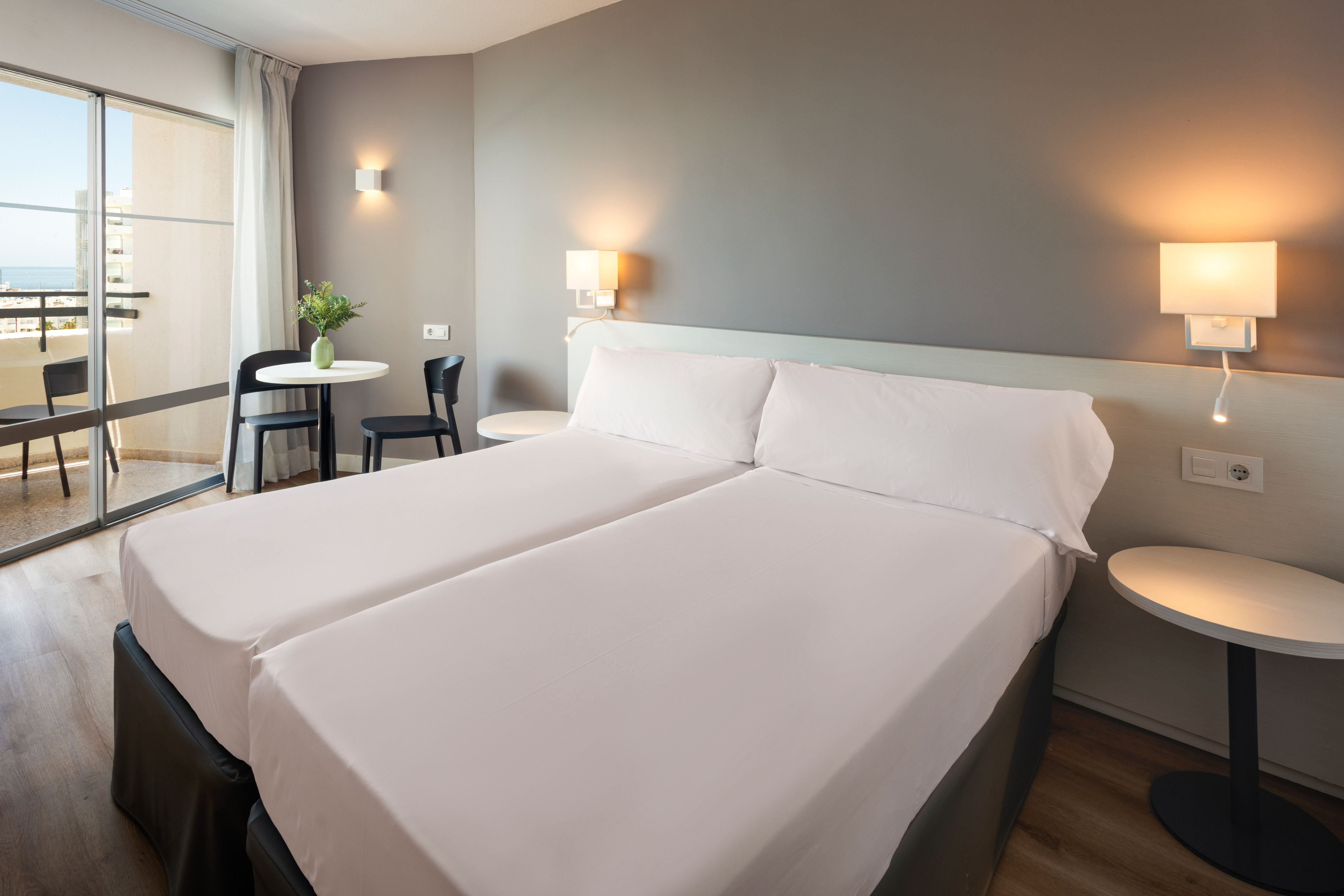 a bed with white sheets and a table with chairs and a lamp