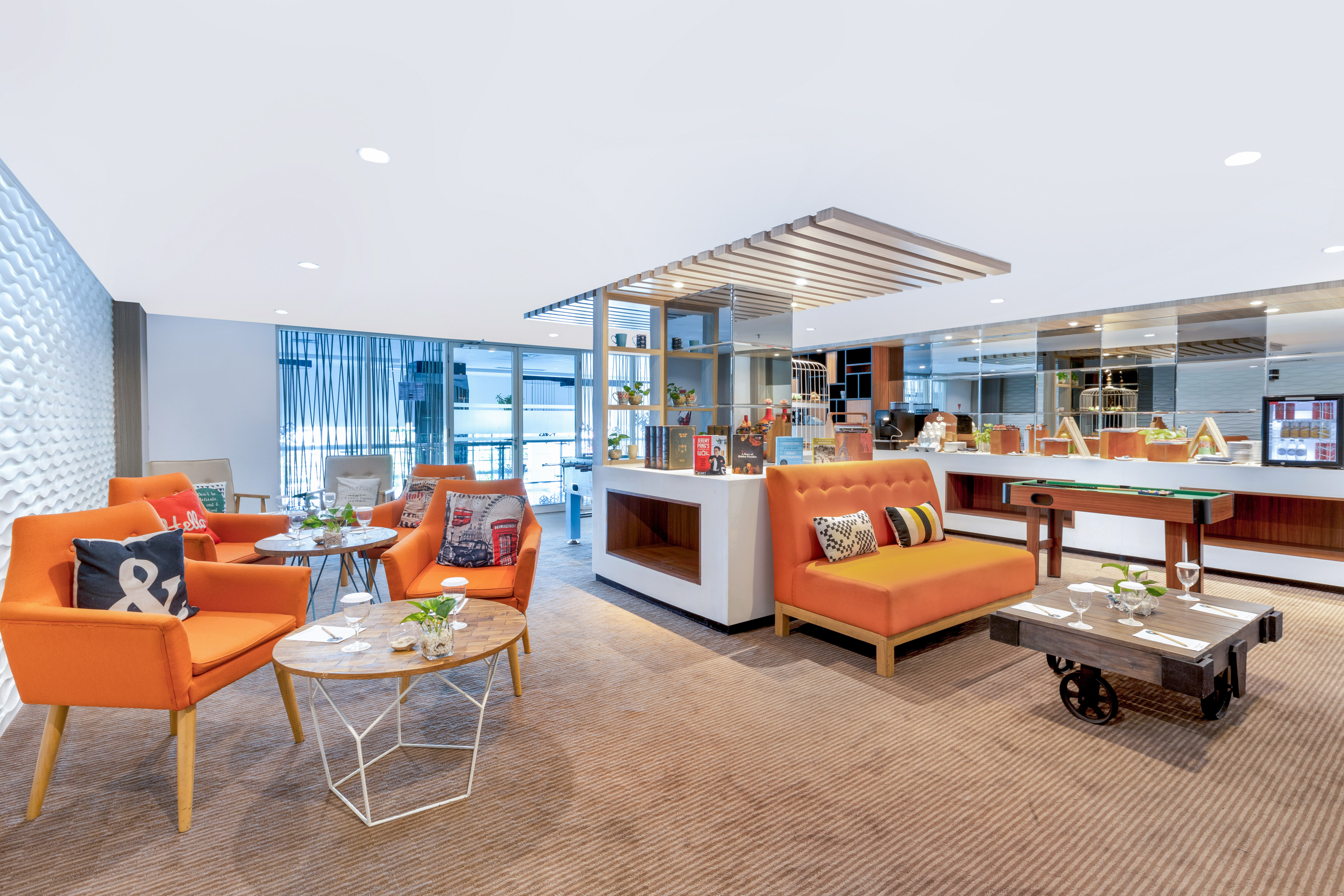 Vibrant hotel lounge with orange seating, coffee tables, and a game area.