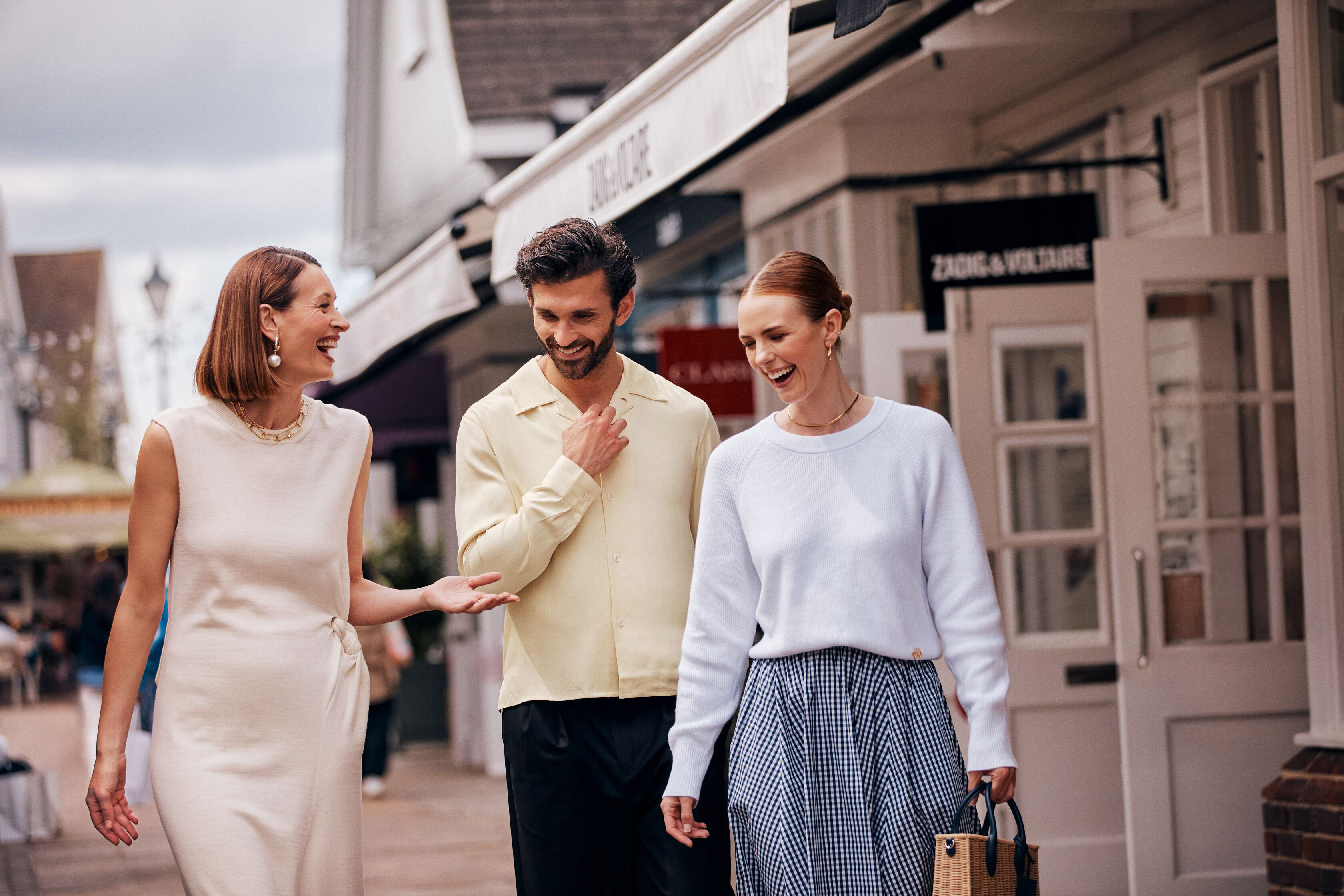 Three happy friends shopping in a luxury outlet village, passing Zadig & Voltaire.