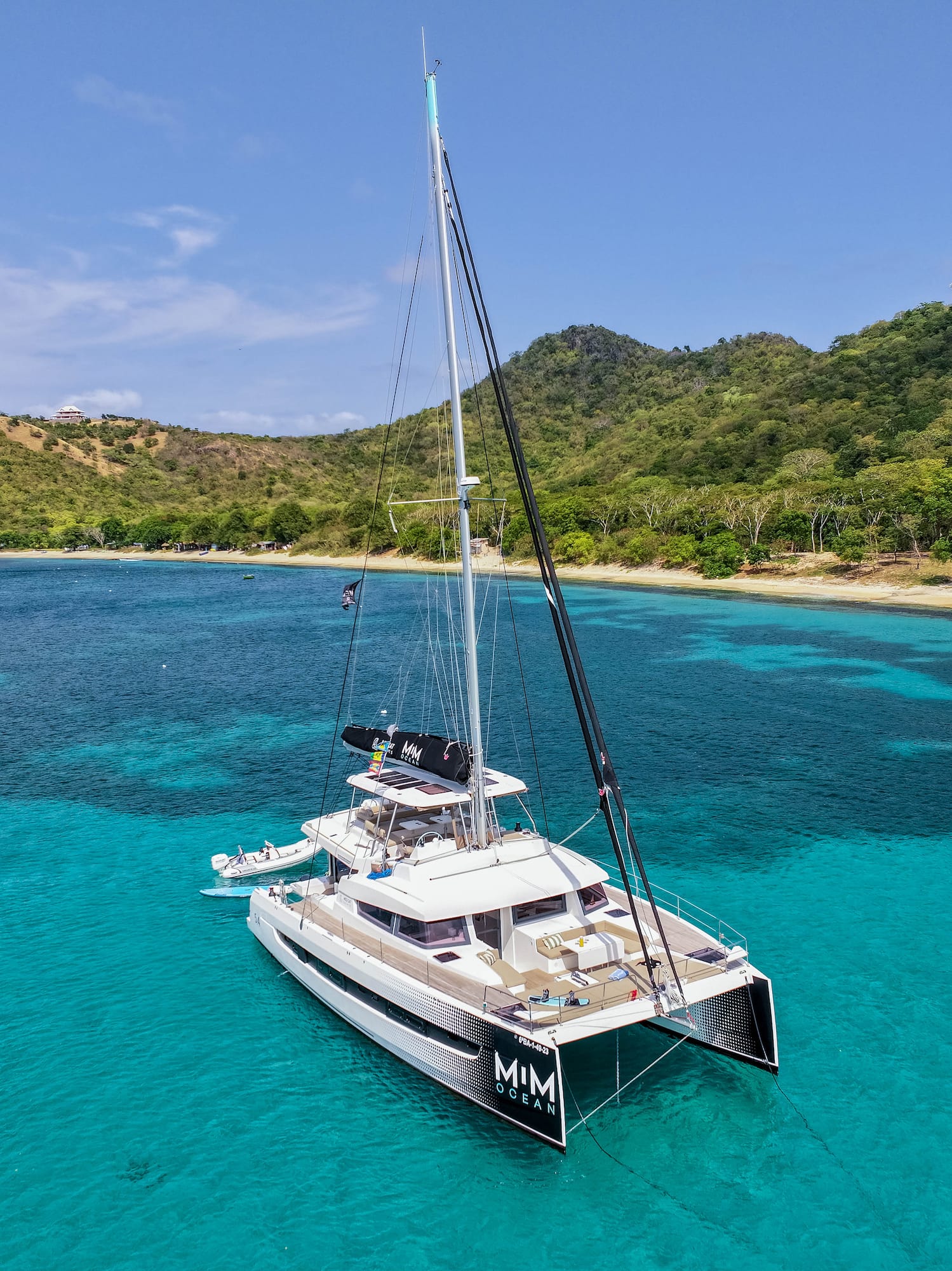 Catamarán de lujo en aguas turquesas del Caribe, con playa y montañas tropicales.