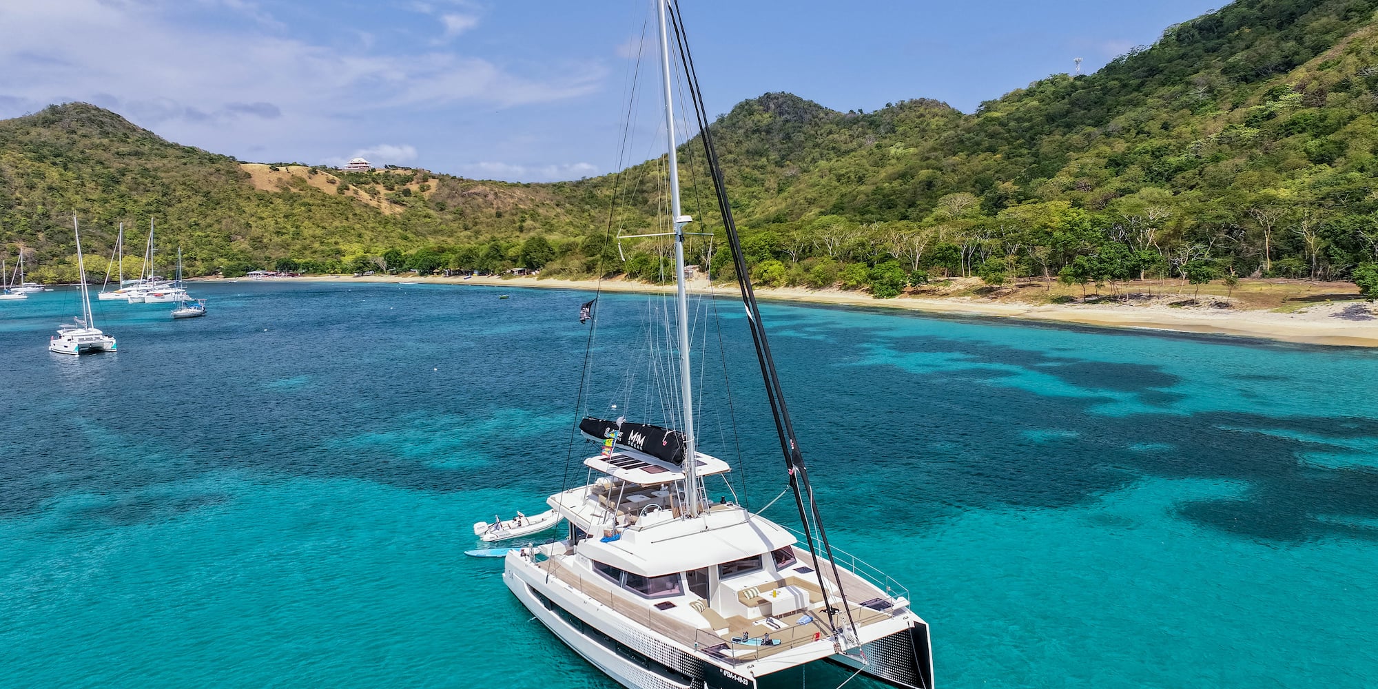 Catamarán de lujo en aguas turquesas del Caribe, con playa y montañas tropicales.