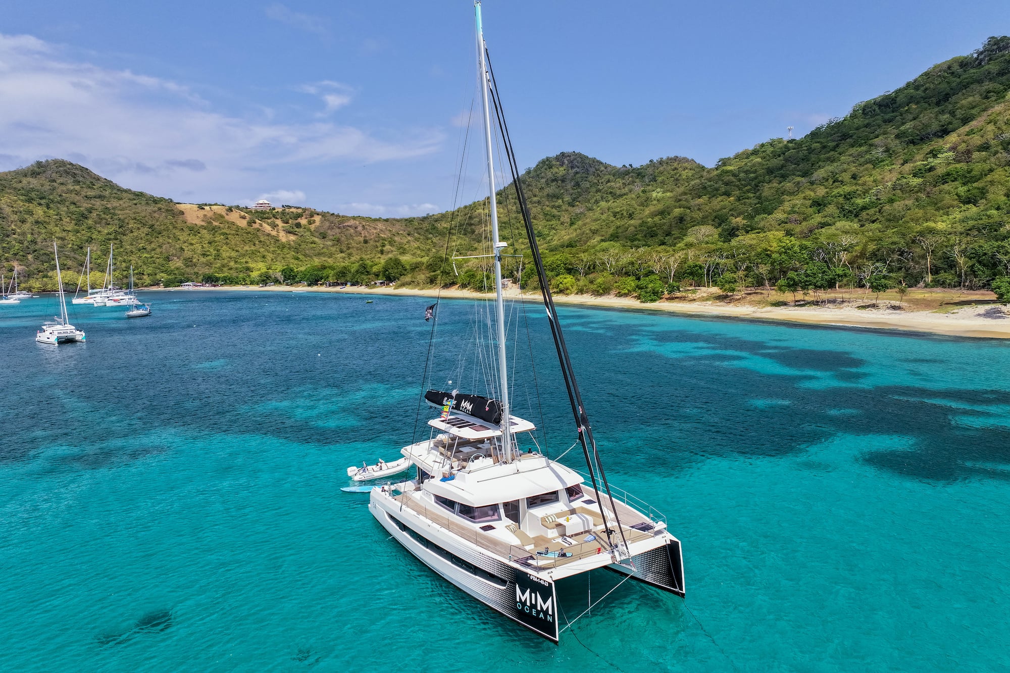 Catamarán de lujo en aguas turquesas del Caribe, con playa y montañas tropicales.