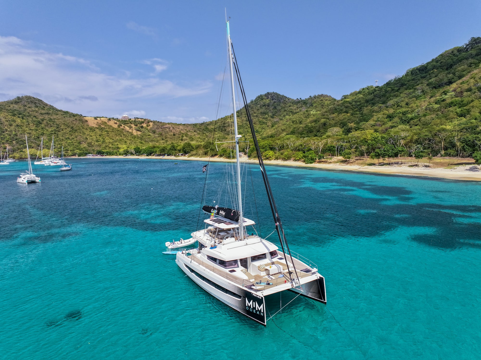 Catamarán de lujo en aguas turquesas del Caribe, con playa y montañas tropicales.