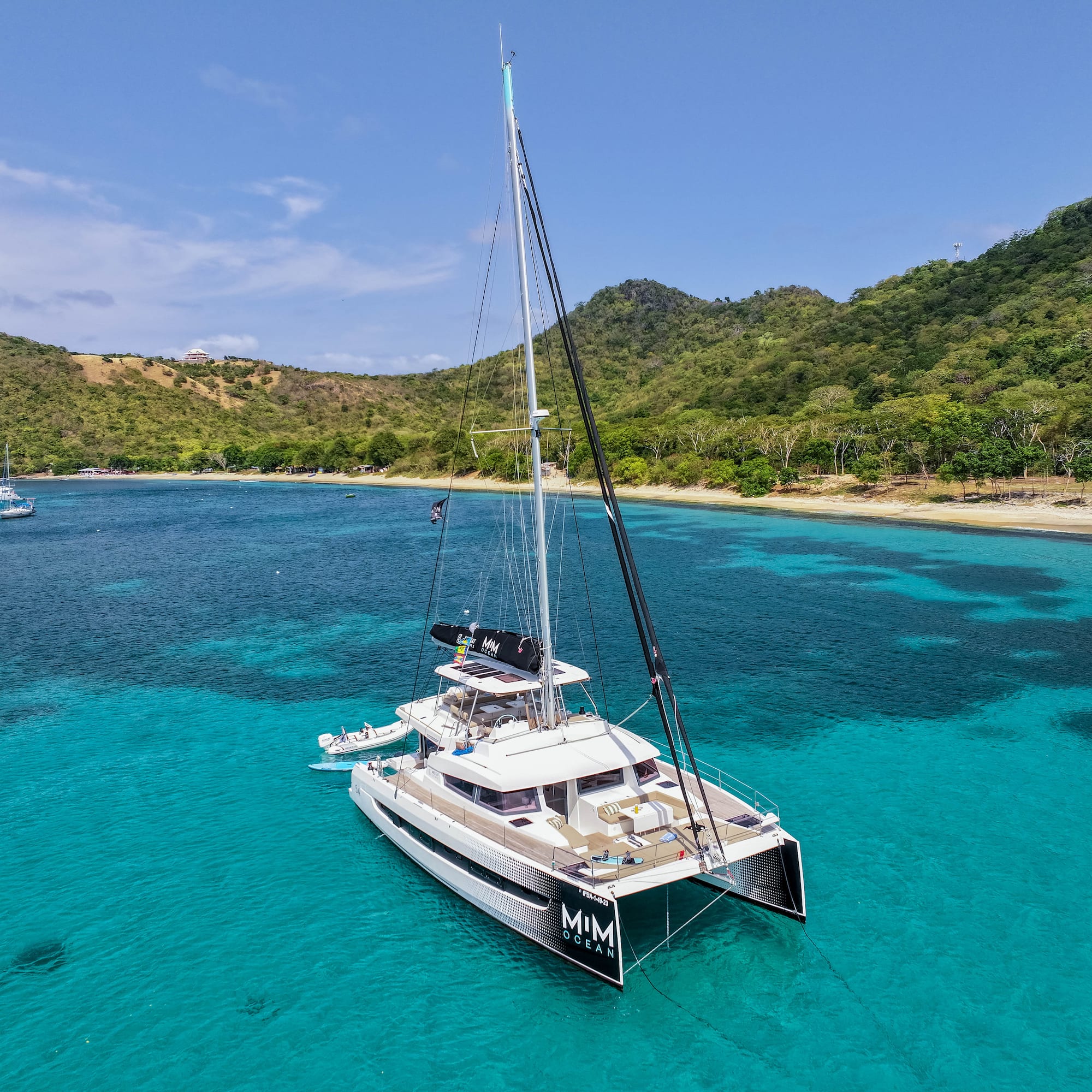 MIM OCEAN catamaran anchored in clear turquoise bay with tropical hills.