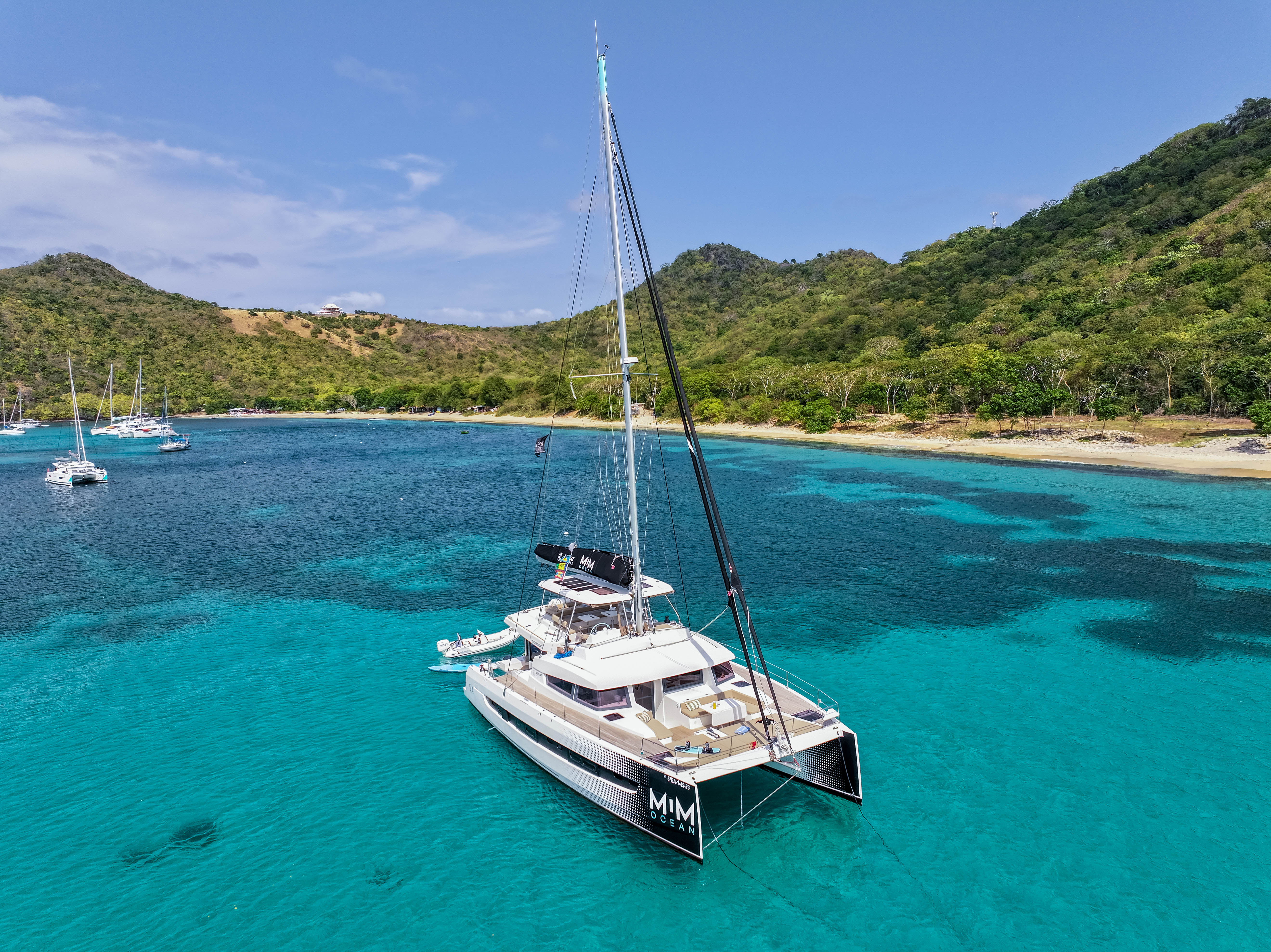 MIM OCEAN catamaran anchored in clear turquoise bay with tropical hills.