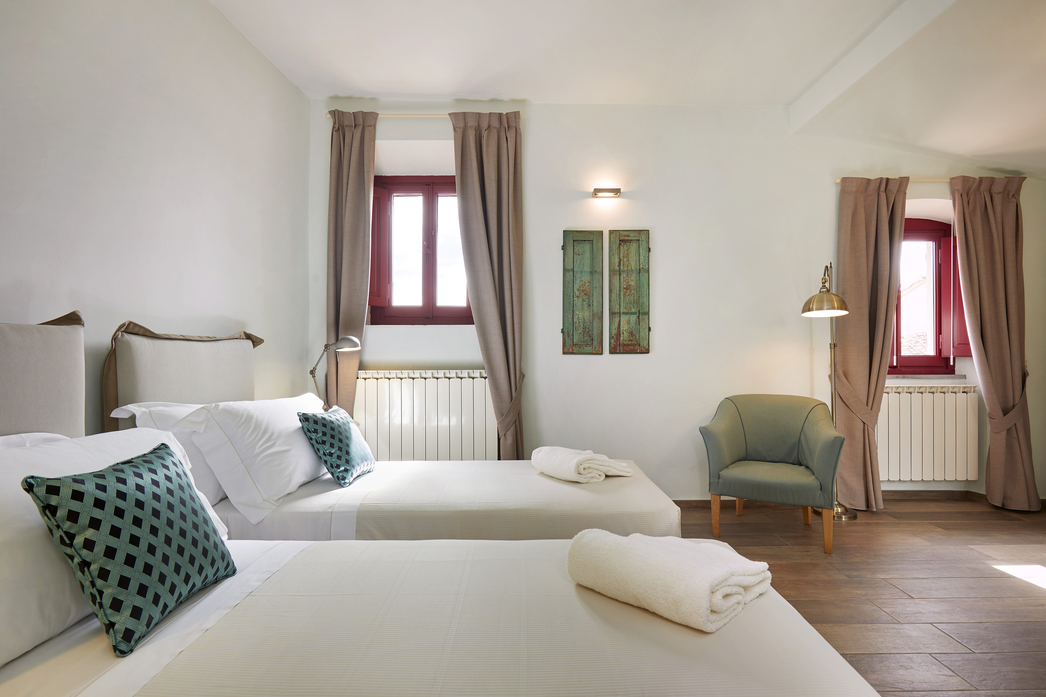 Hotel twin bedroom with two beds, green pillows, red window frames, and wood floors.