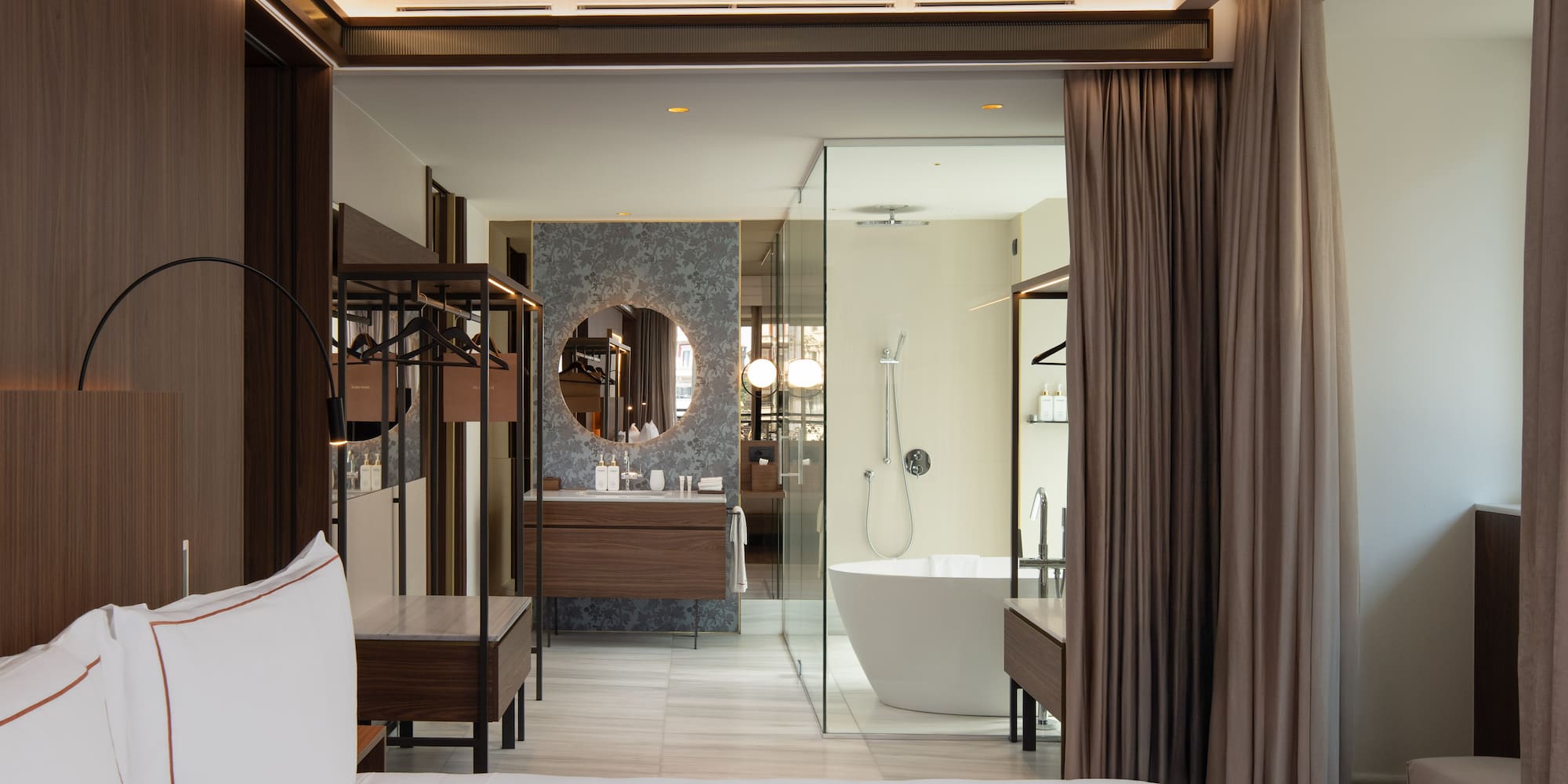 Modern hotel bedroom and open bathroom with freestanding tub, vanity.