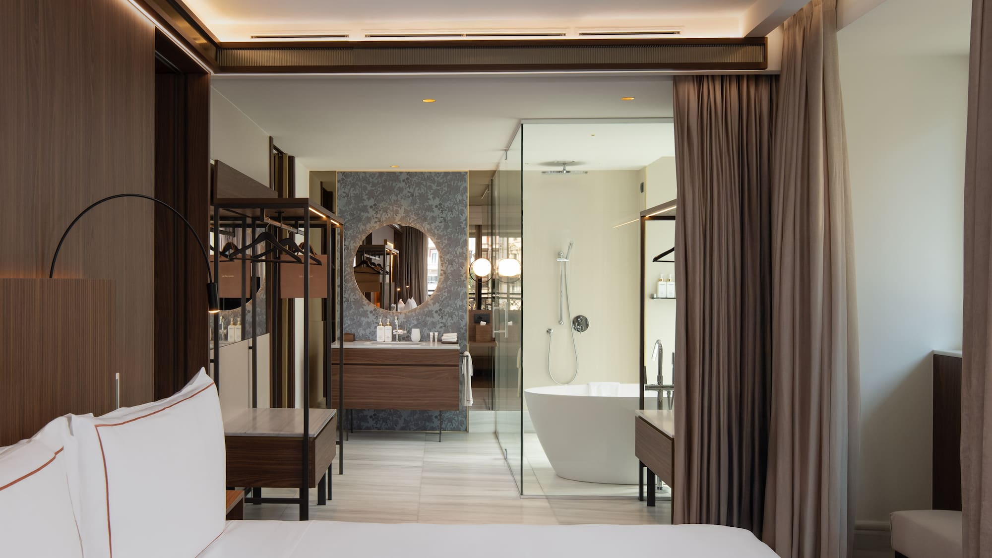 Modern hotel bedroom and open bathroom with freestanding tub, vanity.