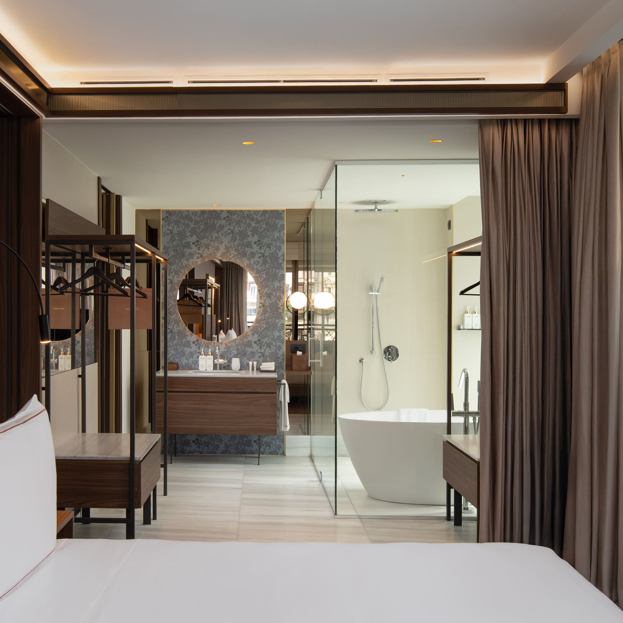 Modern hotel bedroom and open bathroom with freestanding tub, vanity.