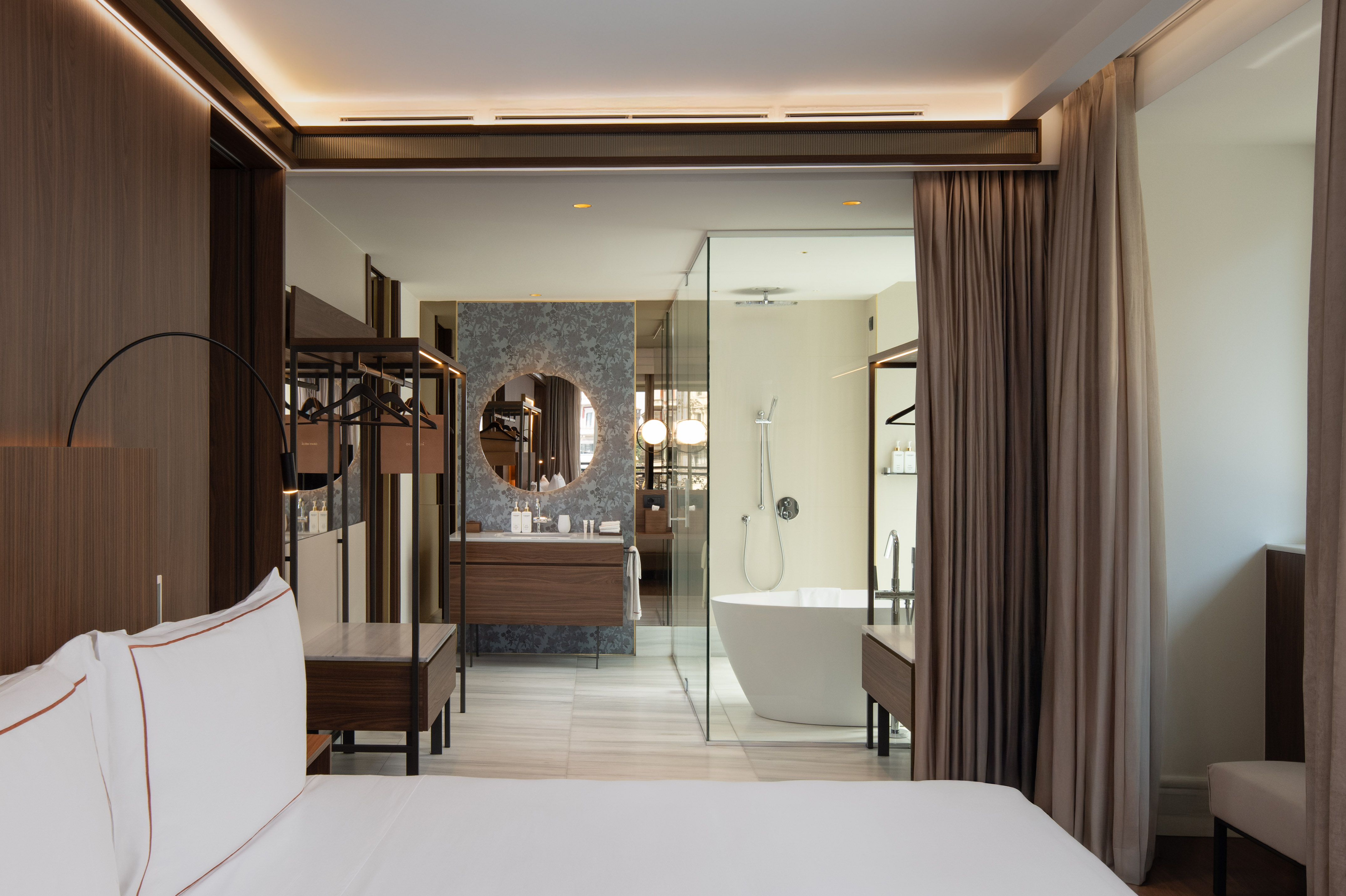 Modern hotel bedroom and open bathroom with freestanding tub, vanity.