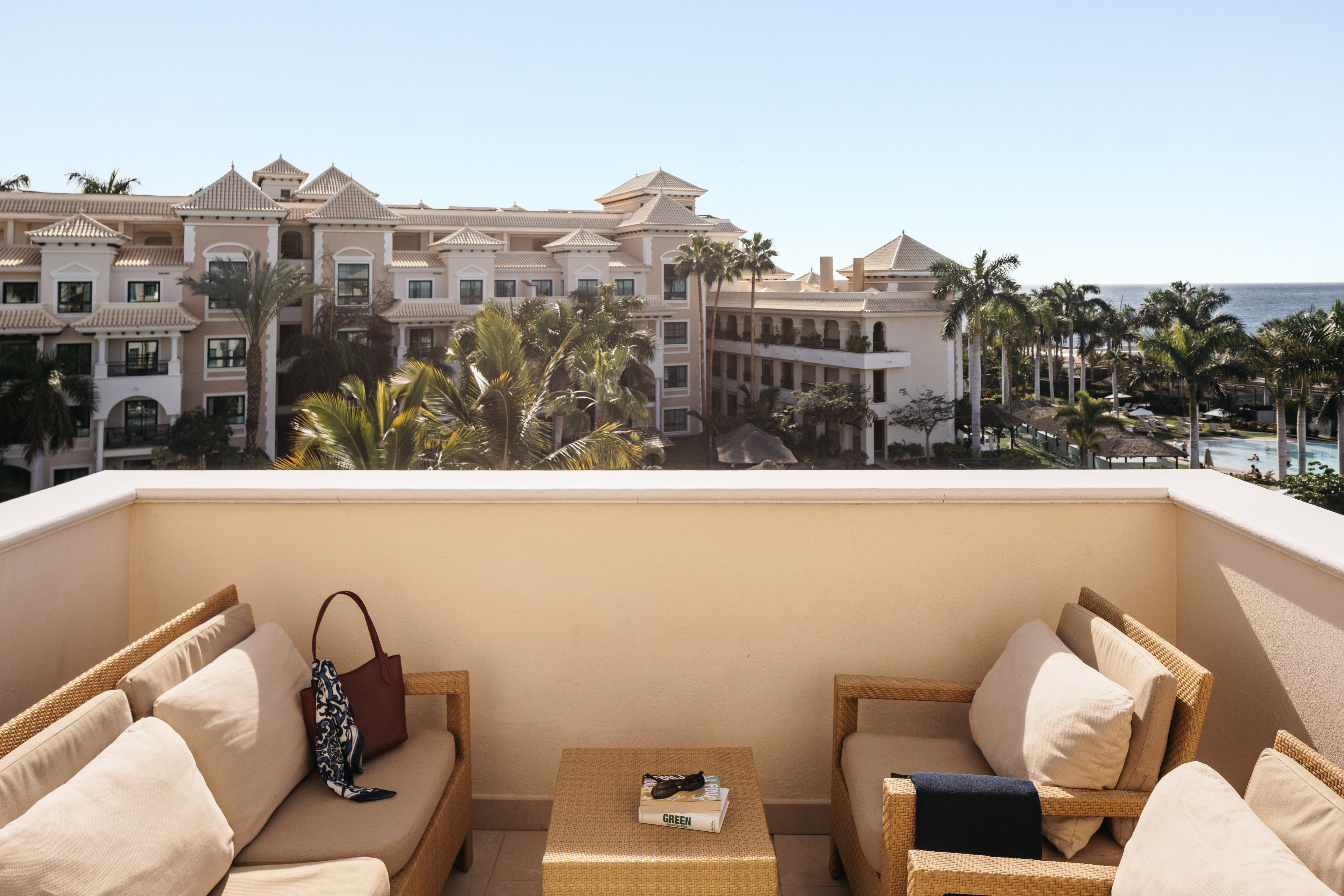 Resort balcony with outdoor seating, palm trees, hotel, and ocean view.