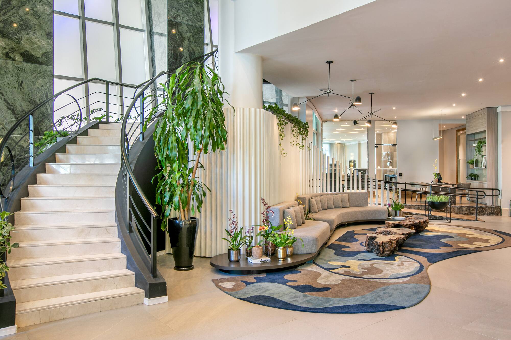 Modern hotel lobby with curved marble staircase, grey sofa, and abstract rug.