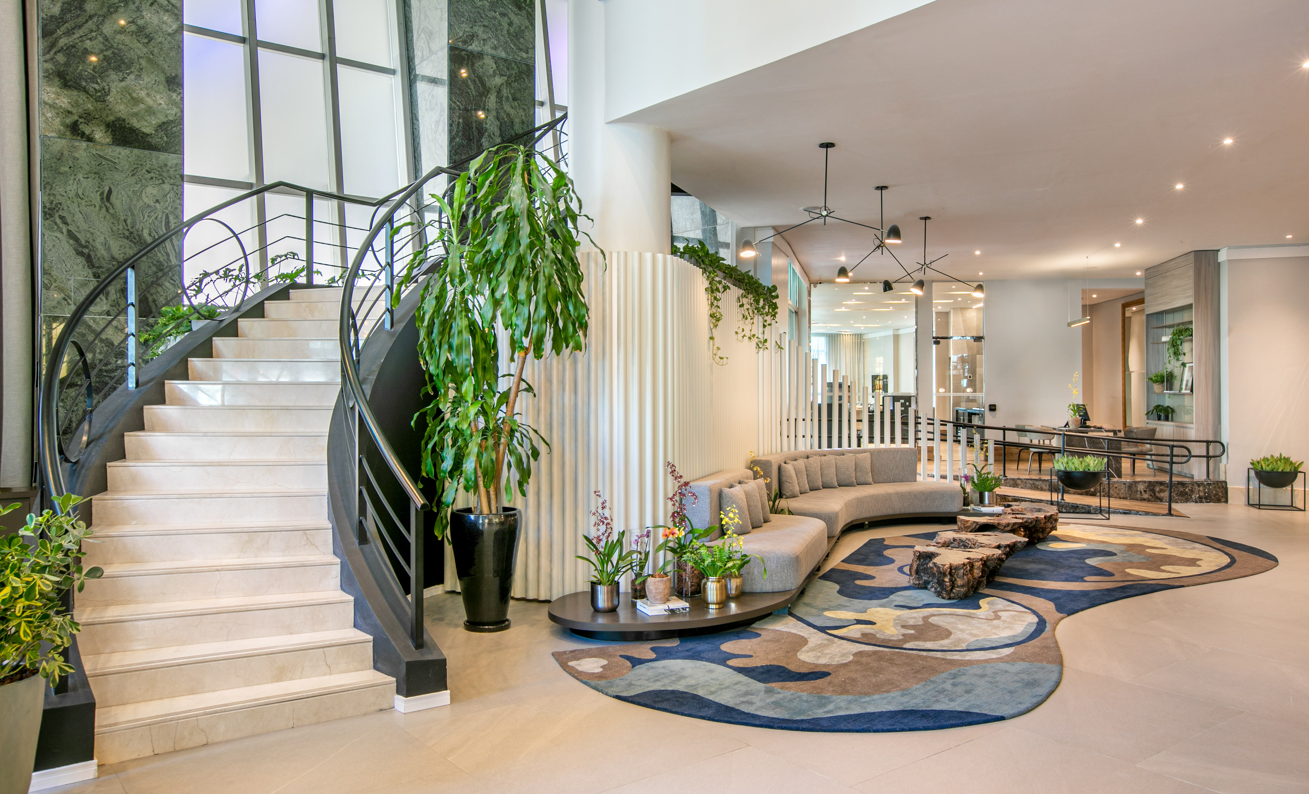 Modern hotel lobby with curved marble staircase, grey sofa, and abstract rug.