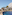 Resort pool with lounge chairs, palm trees, modern hotel, and ocean view.
