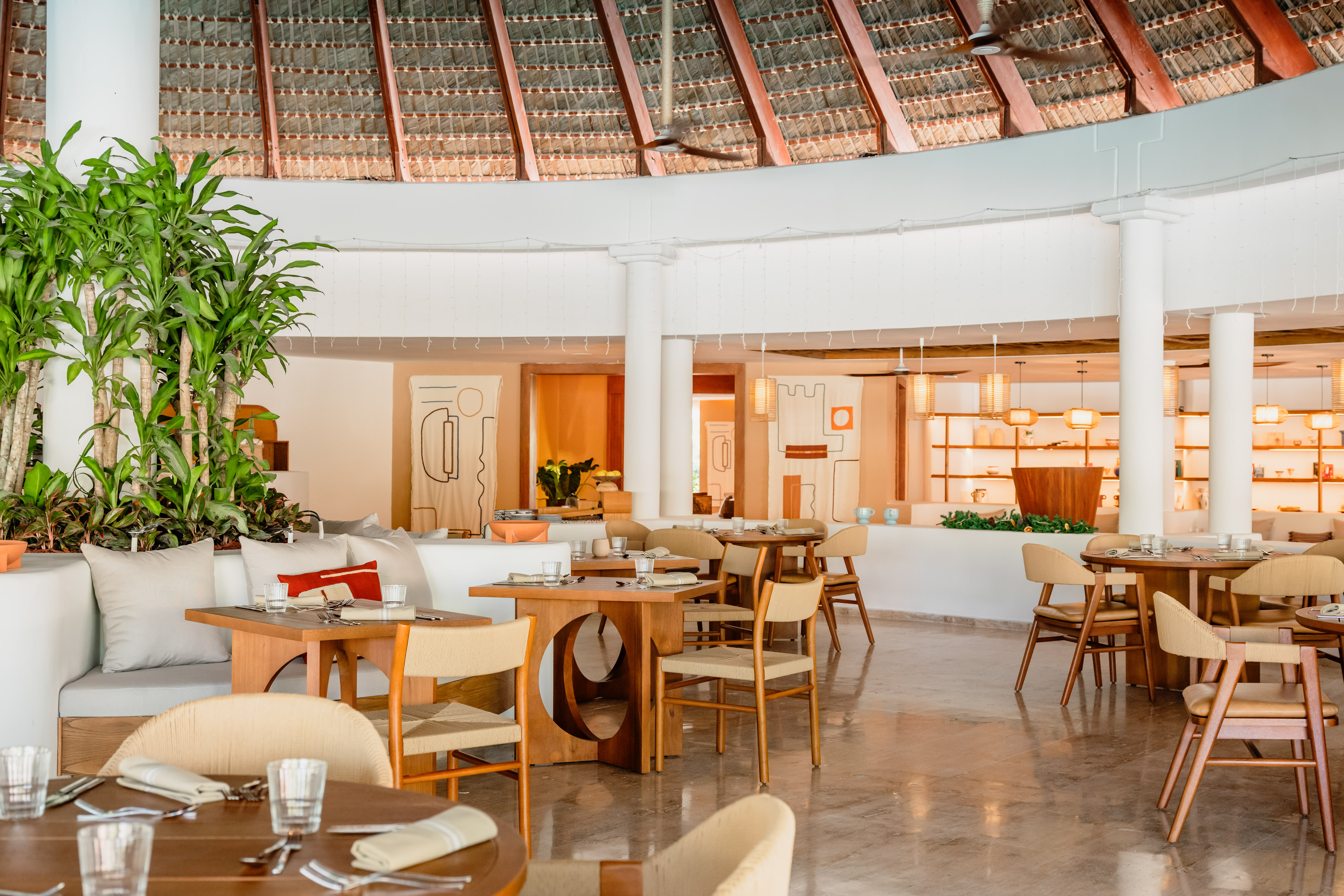 Modern resort dining area with thatched roof, wooden tables, and tropical plants.