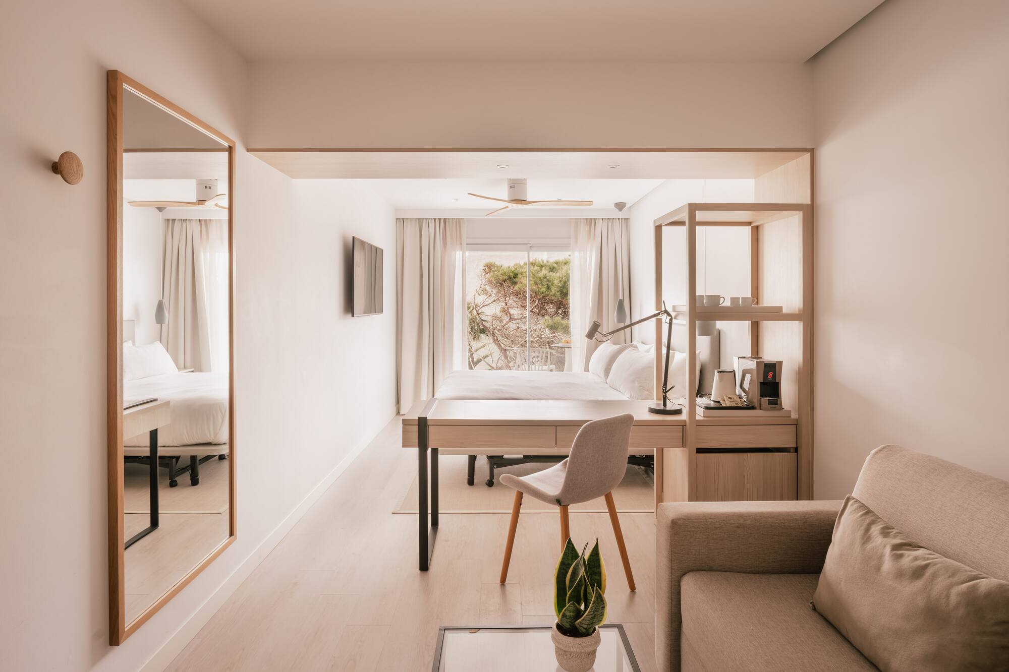 Habitación de hotel moderna y luminosa con cama, escritorio y vistas al exterior.