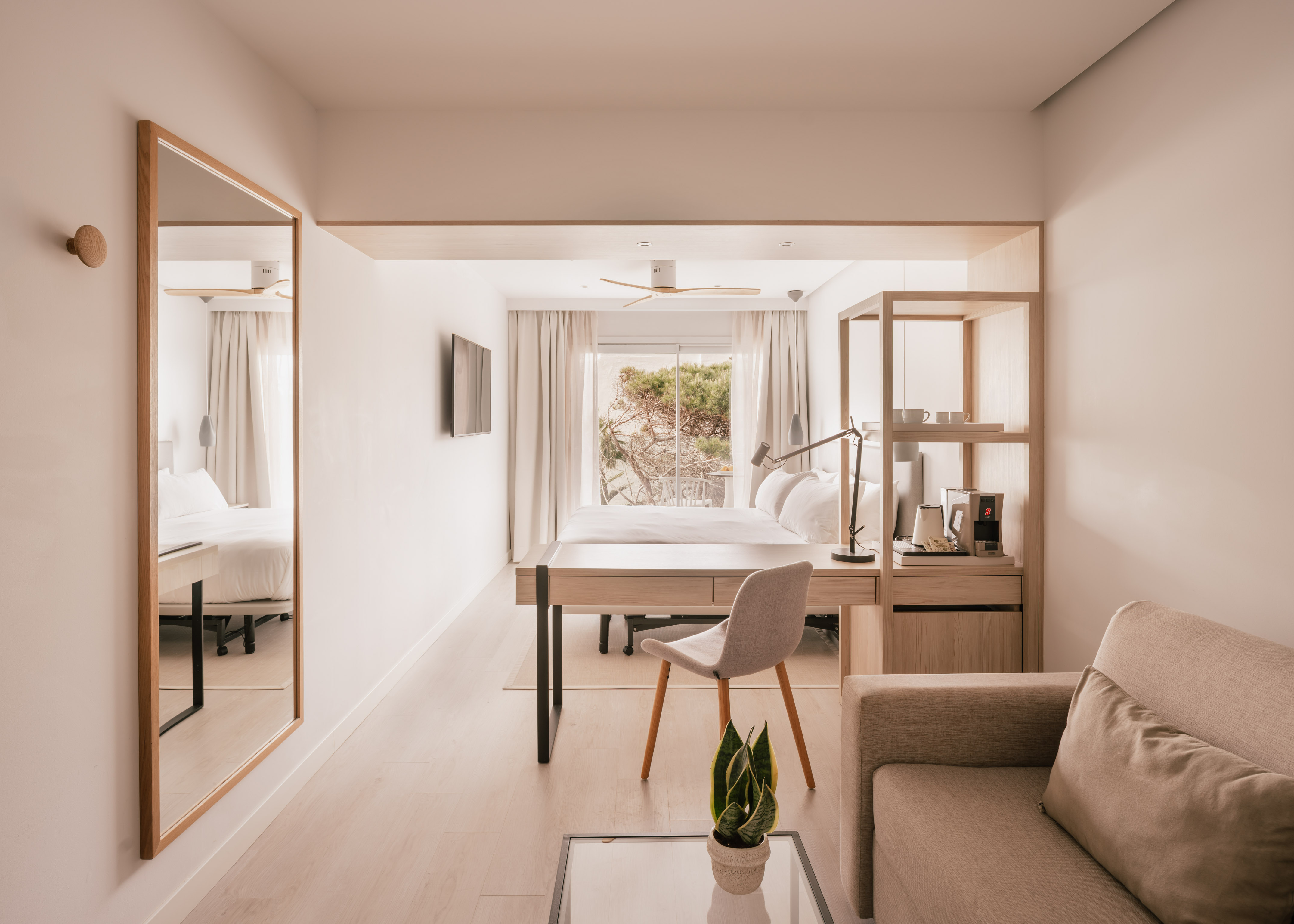 Habitación de hotel moderna y luminosa con cama, escritorio y vistas al exterior.