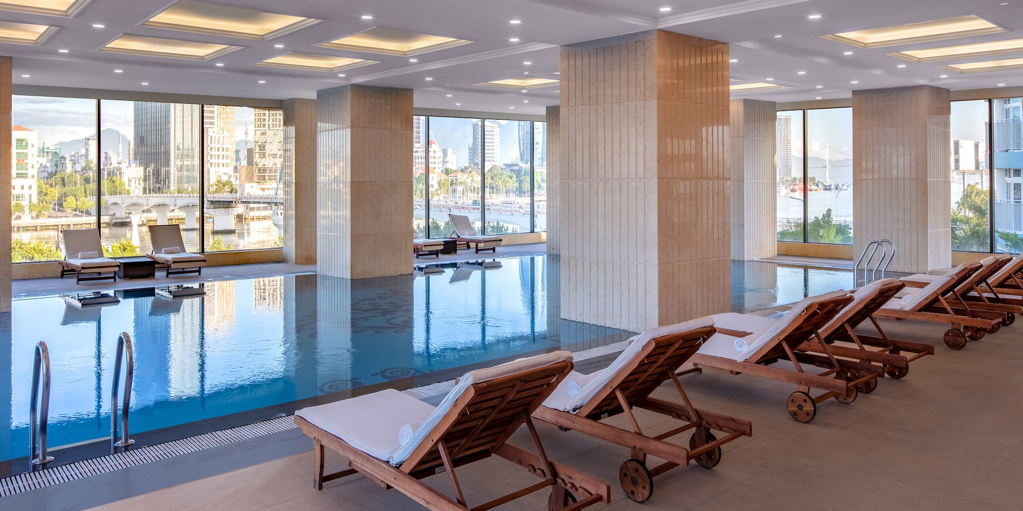 a pool with chairs in a room with windows and a city view