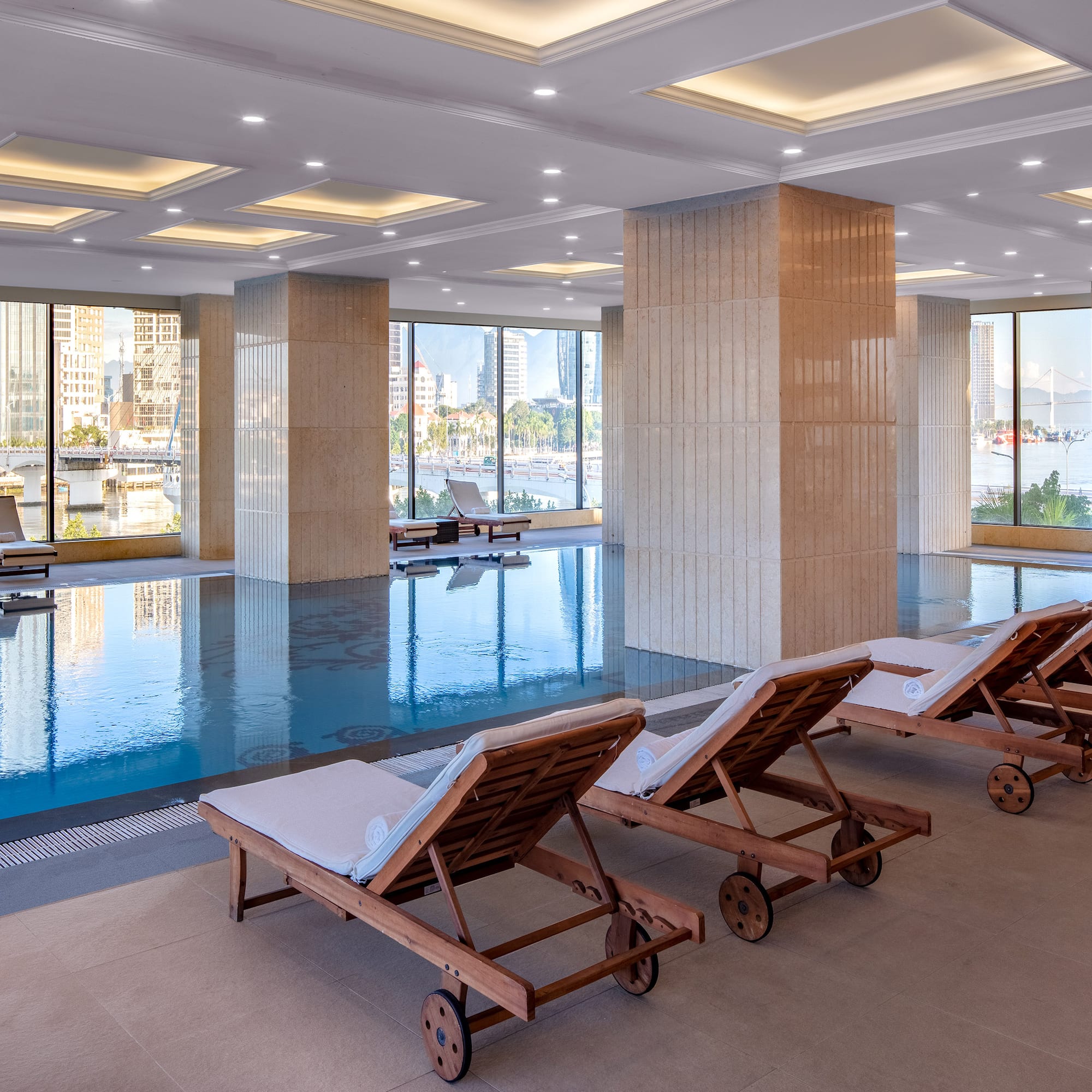 a pool with chairs in a room with windows and a city view