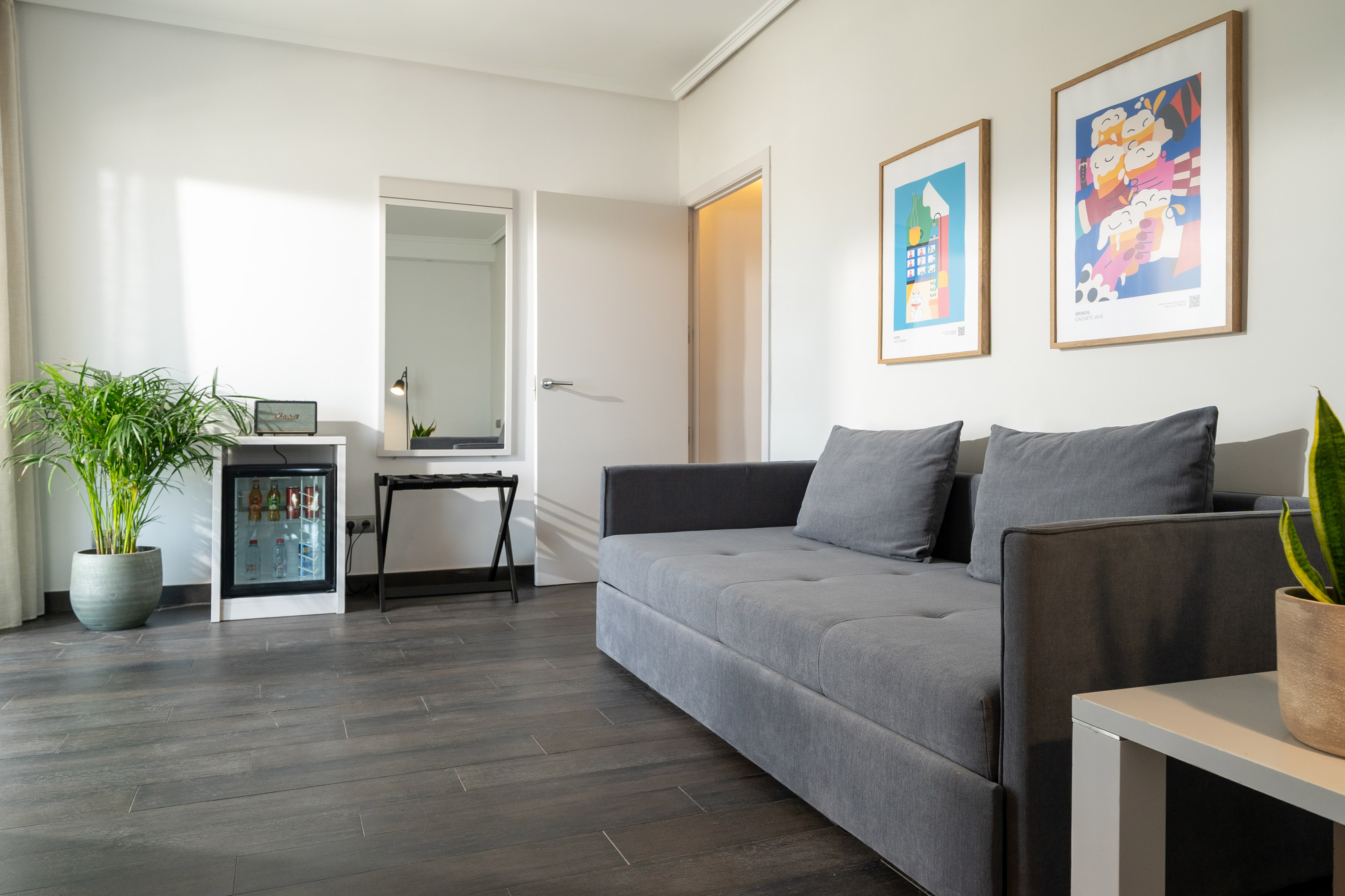 Contemporary living room with grey sofa, minibar, abstract art, and potted plants.