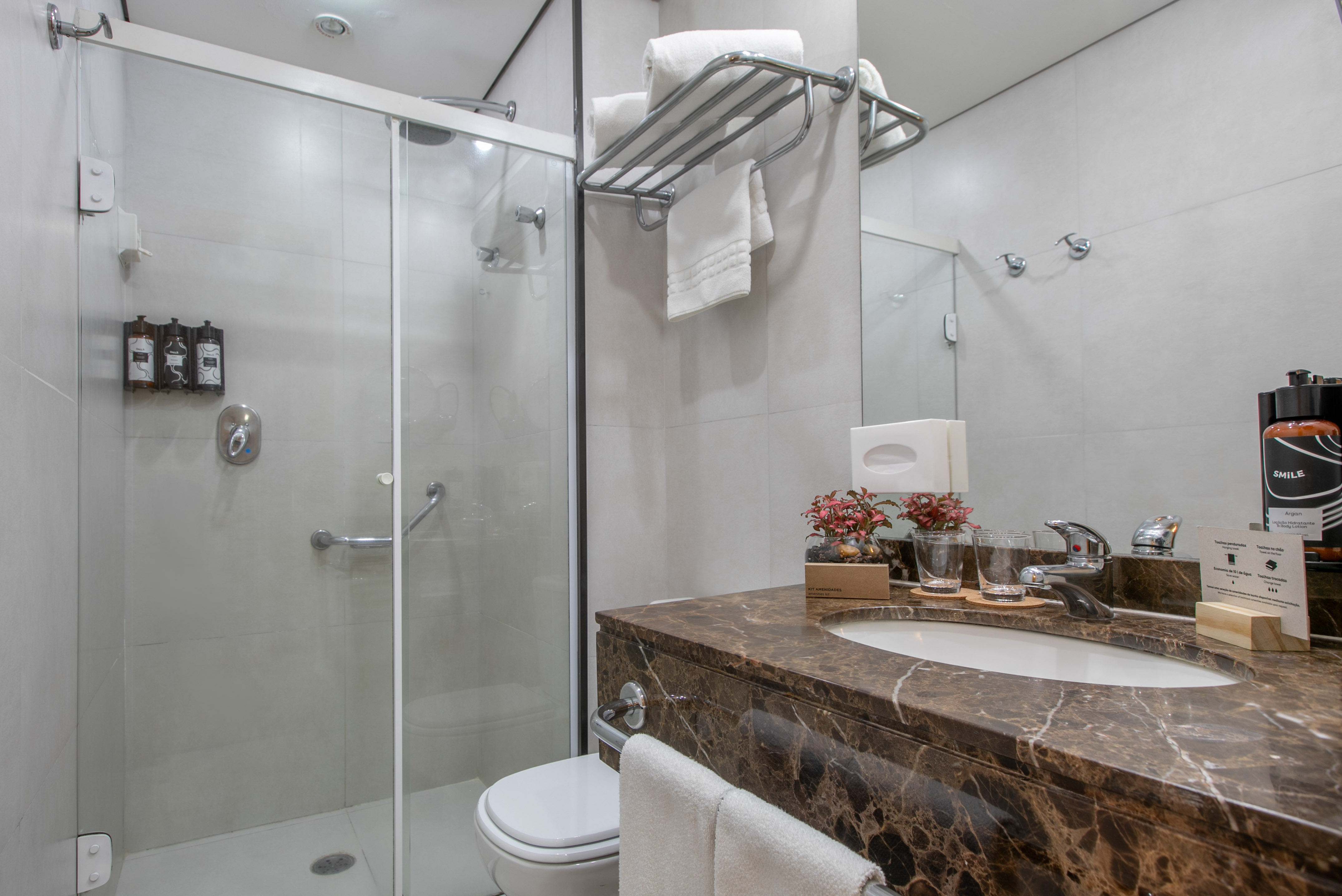 Modern hotel bathroom featuring glass shower, brown marble vanity, and toilet.