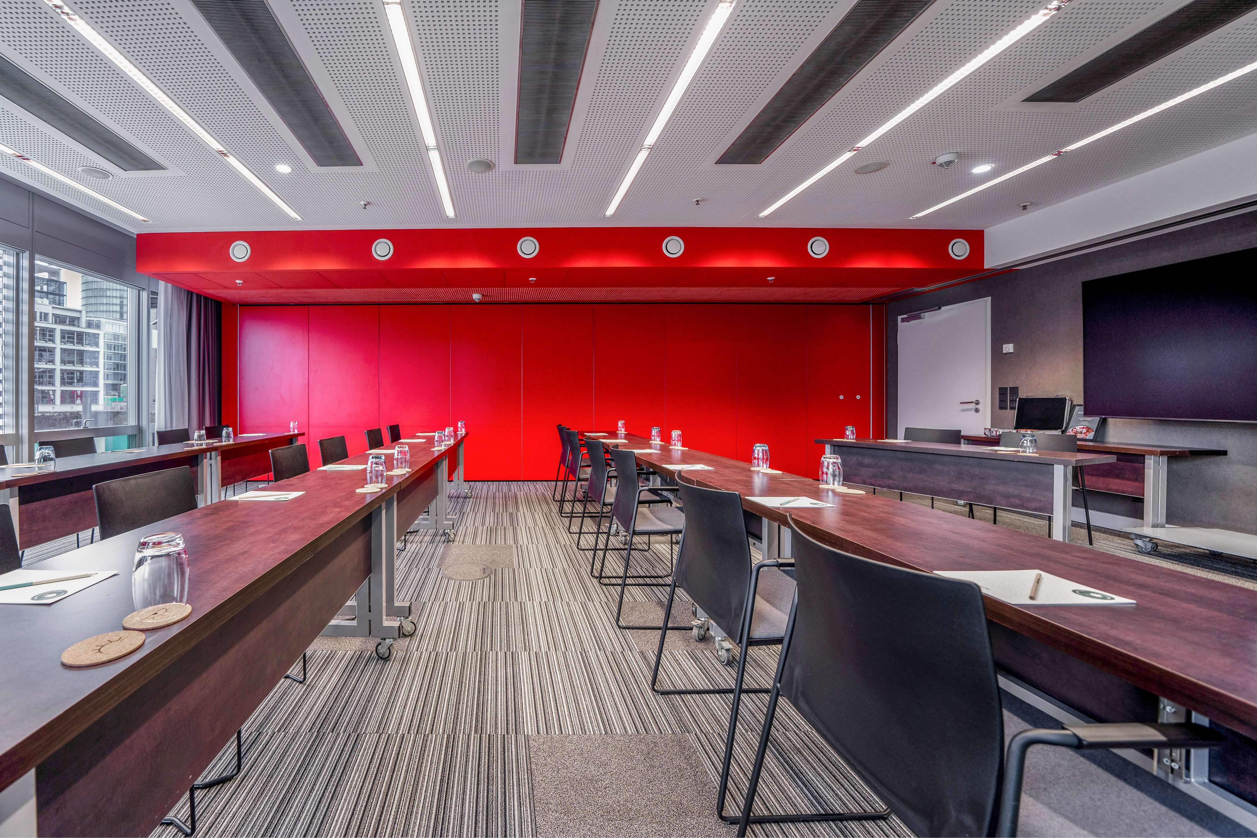 Modern conference room with red accent wall, long tables, and striped carpet.