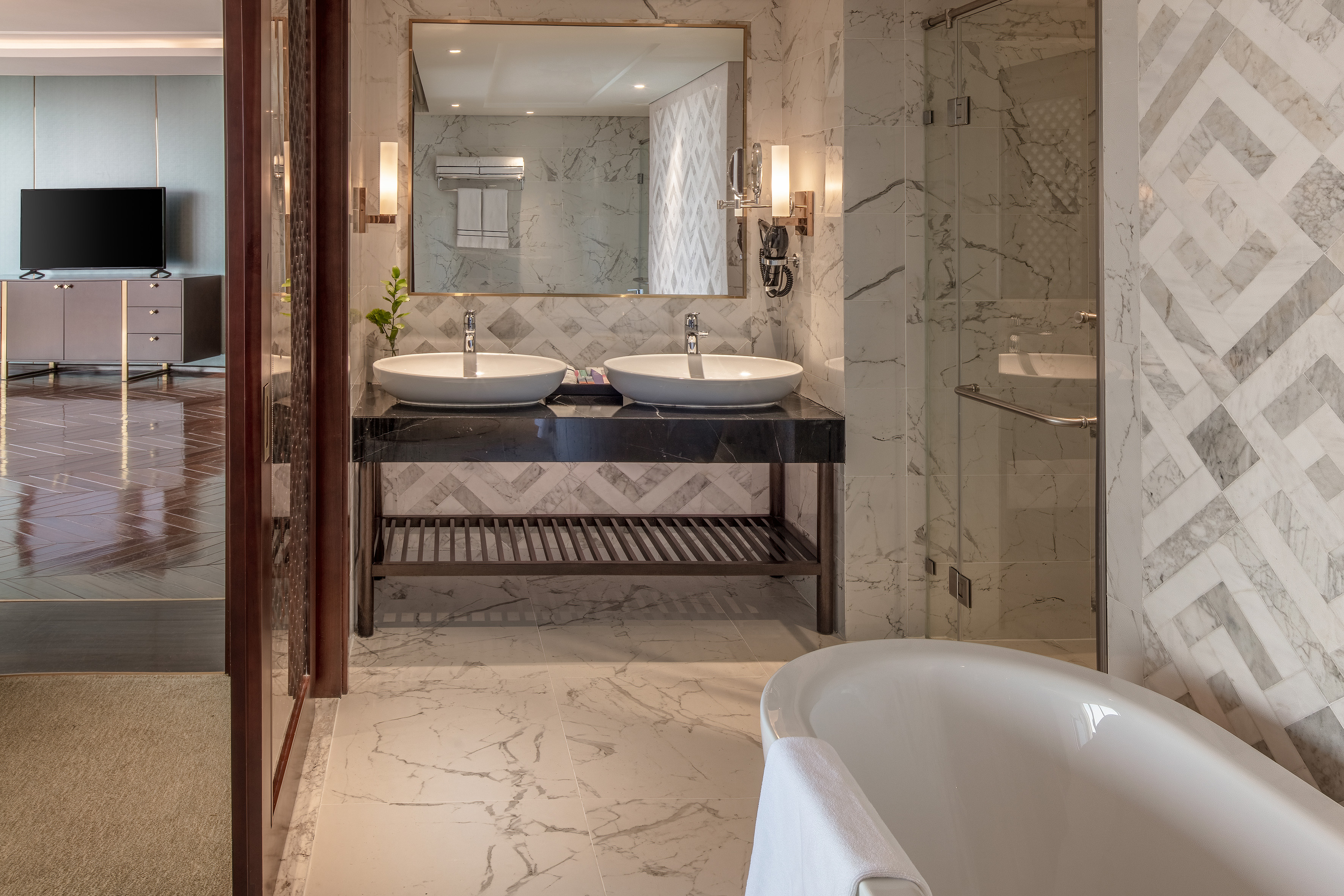 Elegant hotel bathroom with marble, dual vanity, freestanding bathtub, and glass shower.
