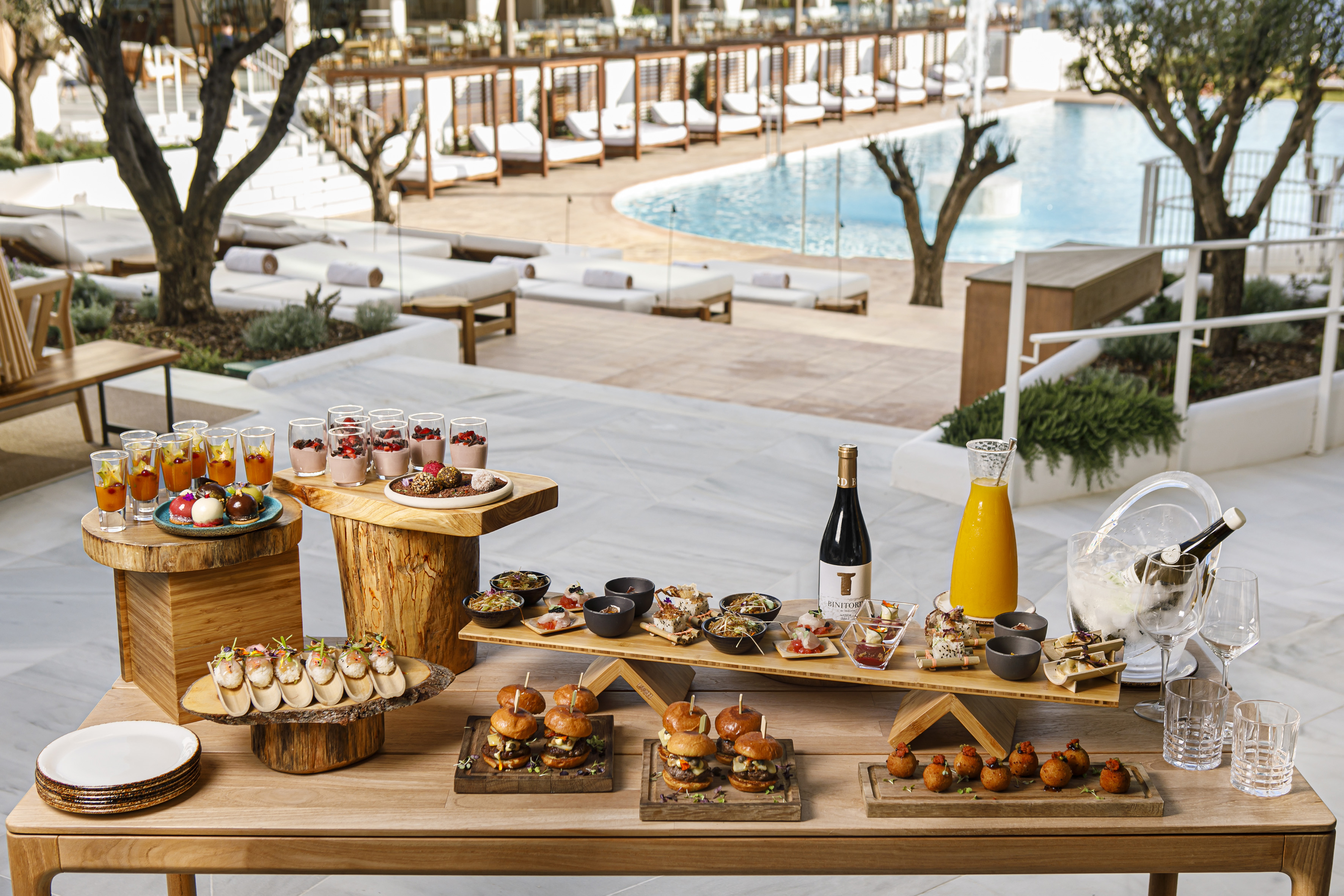 Luxury outdoor buffet with appetizers, desserts, wine, and a resort pool.