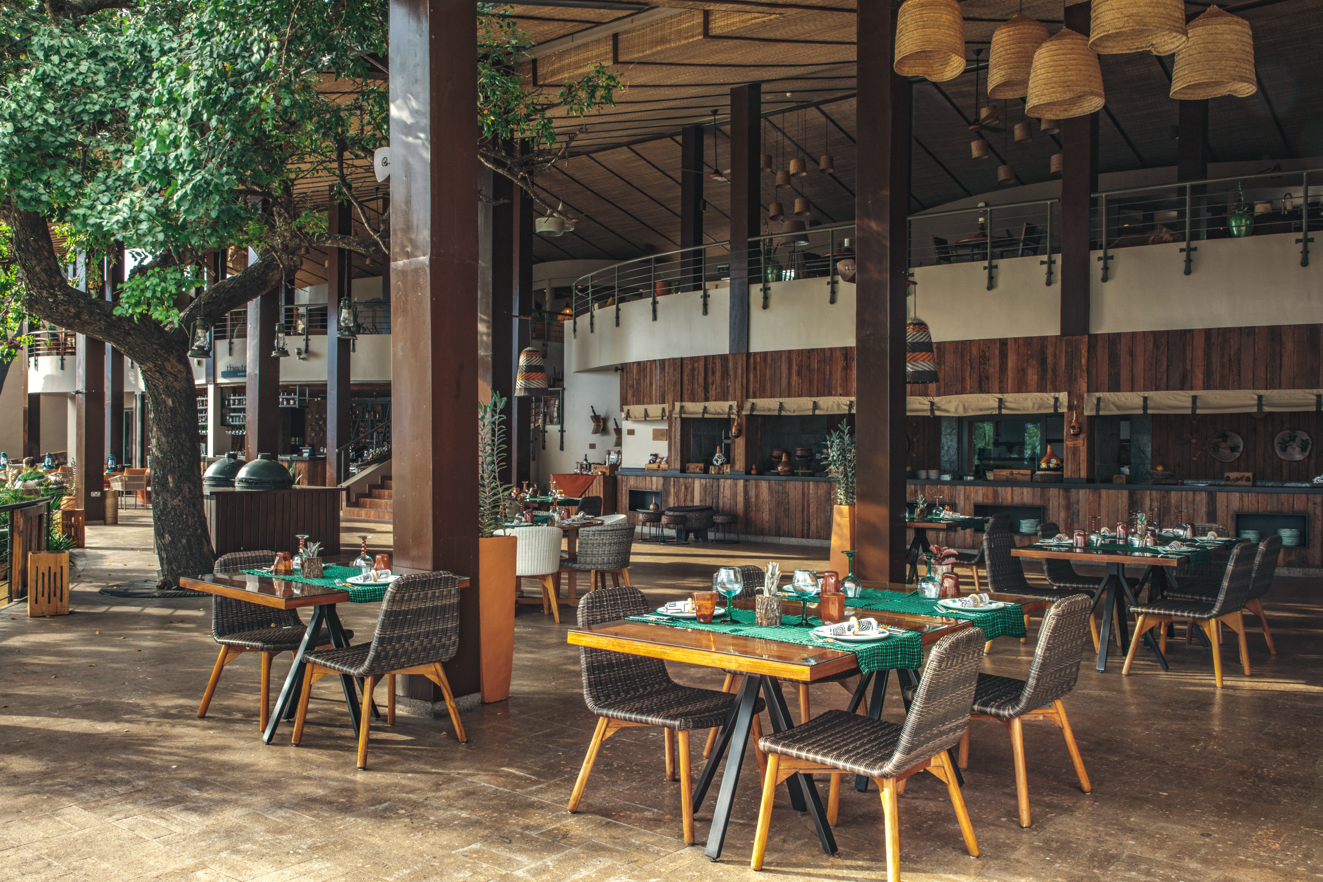 Tropical resort restaurant with wooden tables, chairs, and lush tree.