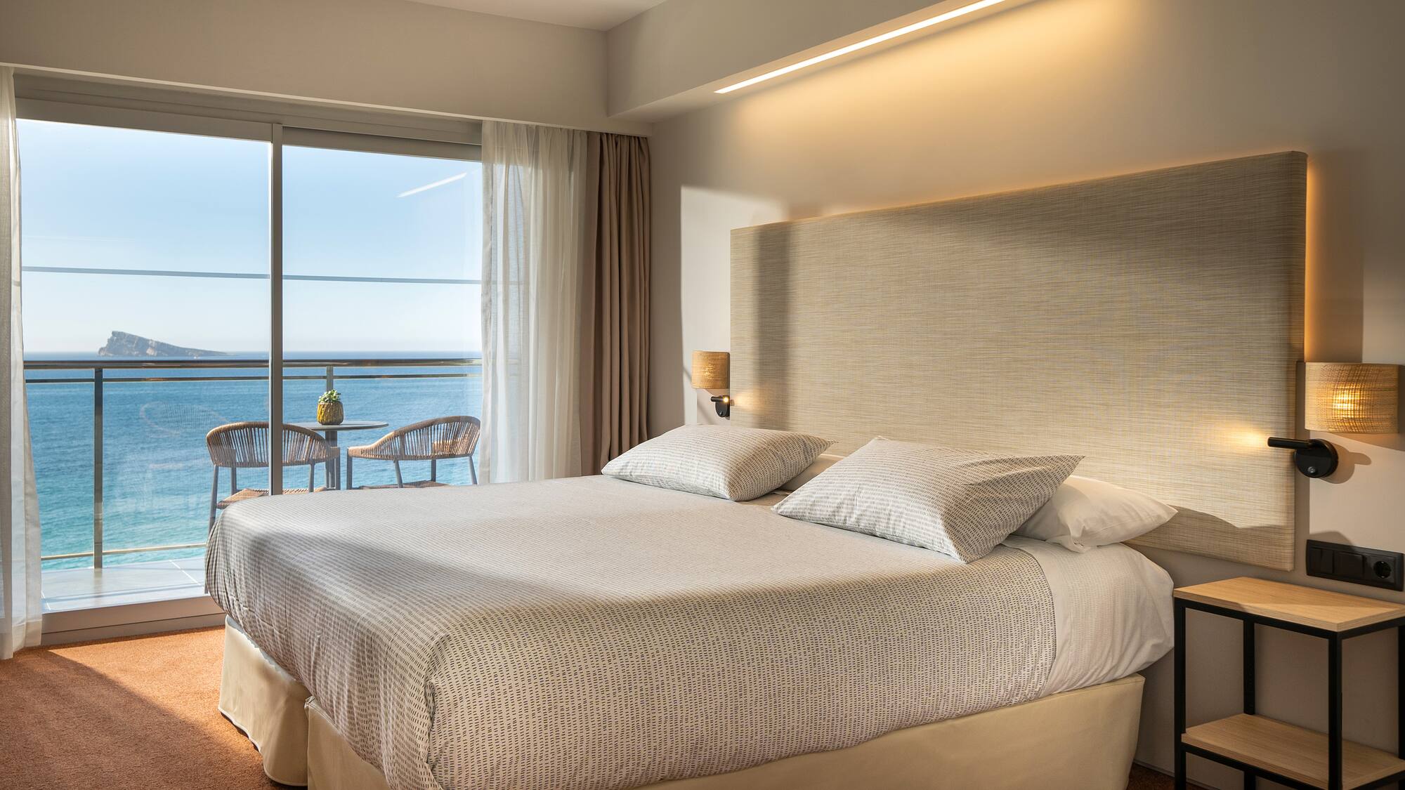 a bed with a large headboard and a glass door overlooking the ocean
