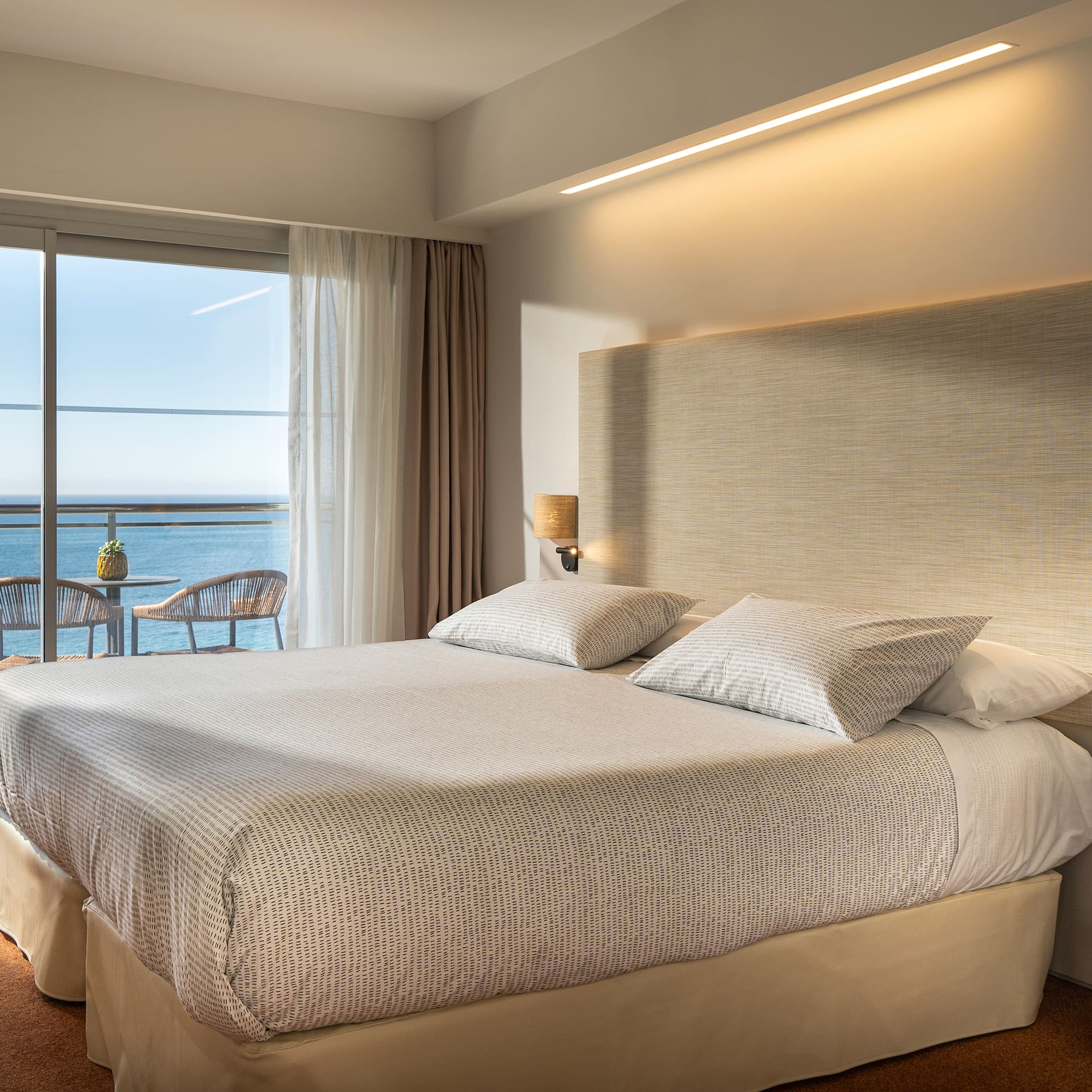 a bed with a large headboard and a glass door overlooking the ocean
