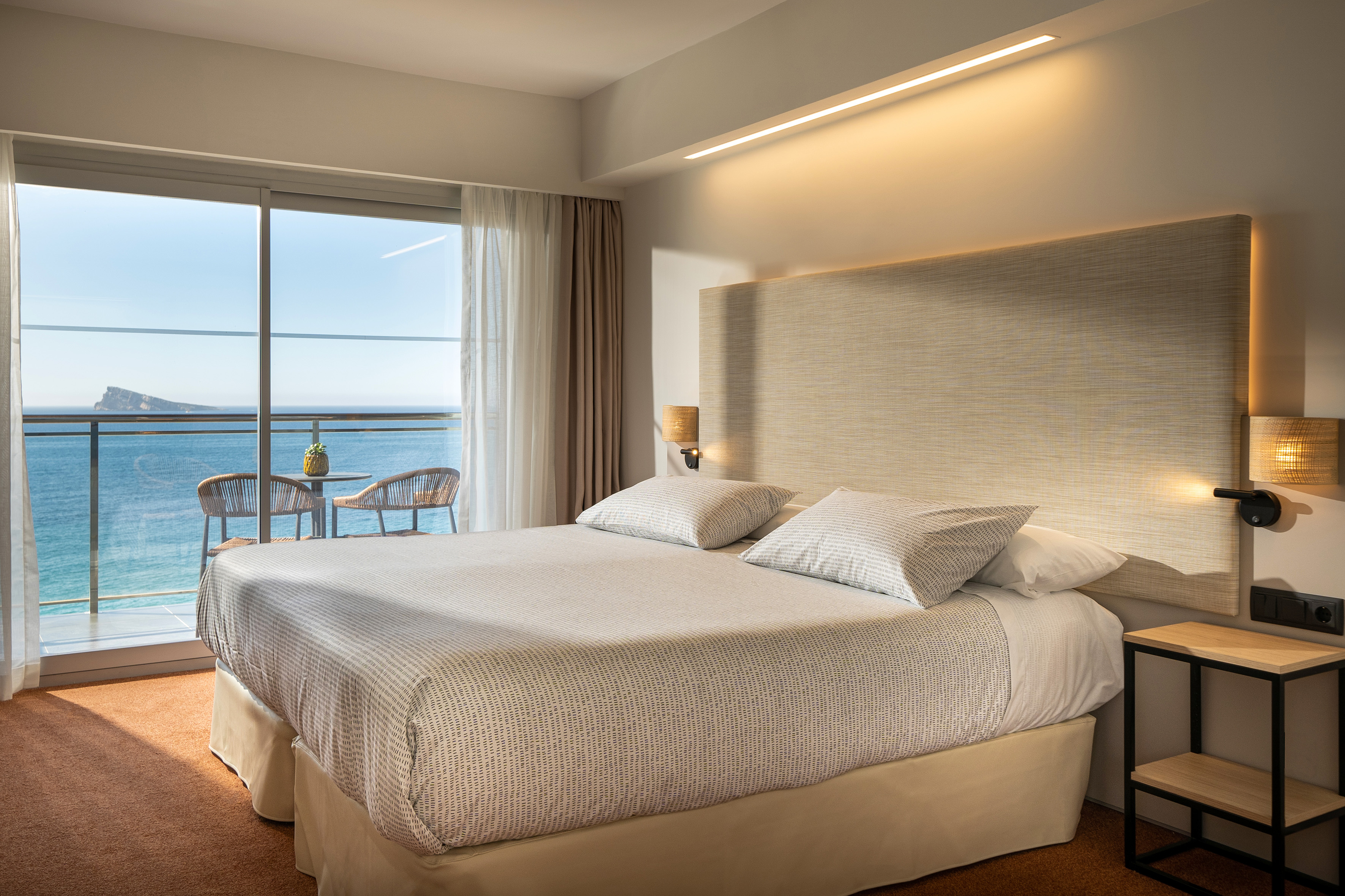 Bright hotel room with balcony overlooking the ocean and island.
