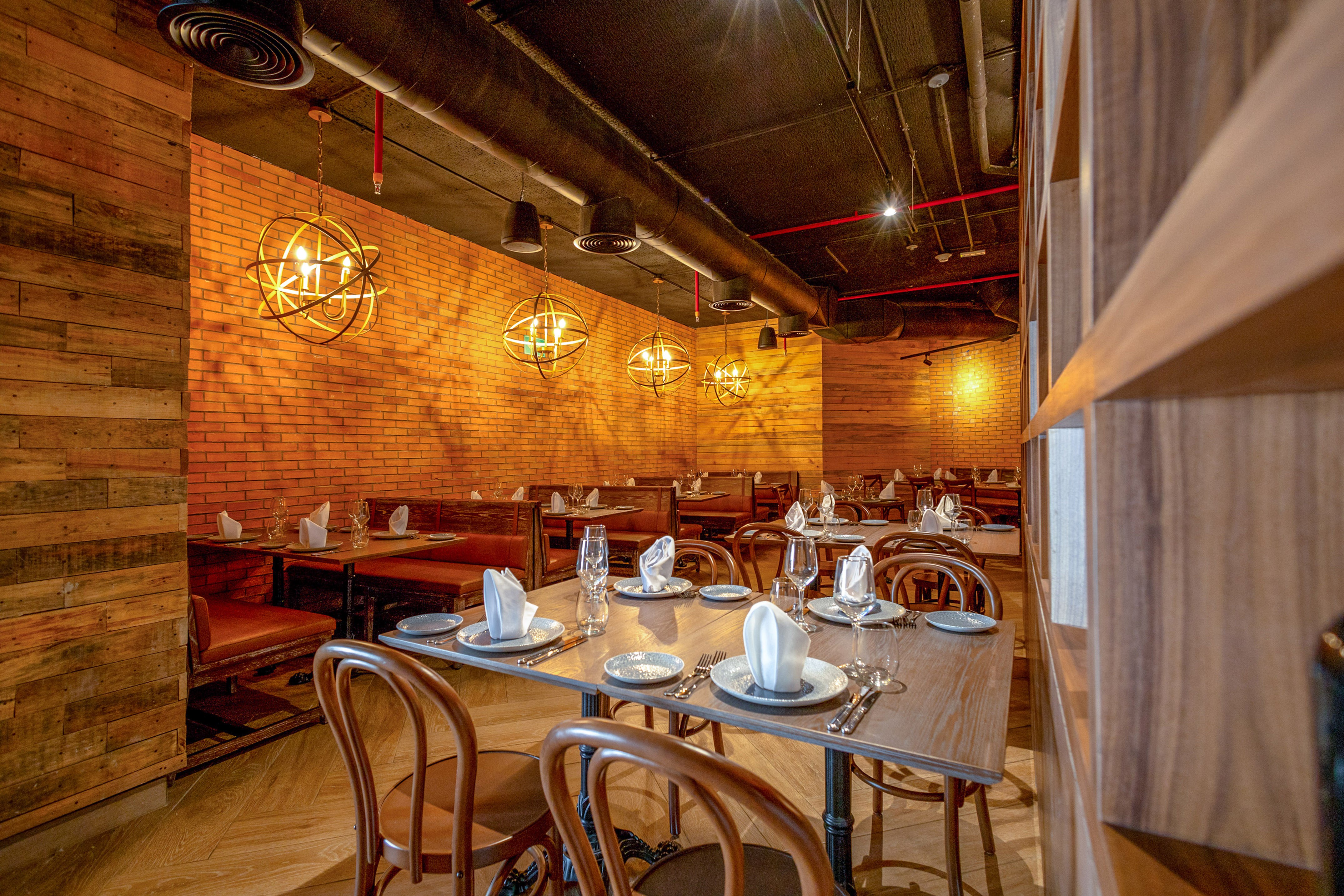 Restaurant dining area with brick wall, wooden tables, and spherical pendant lights.