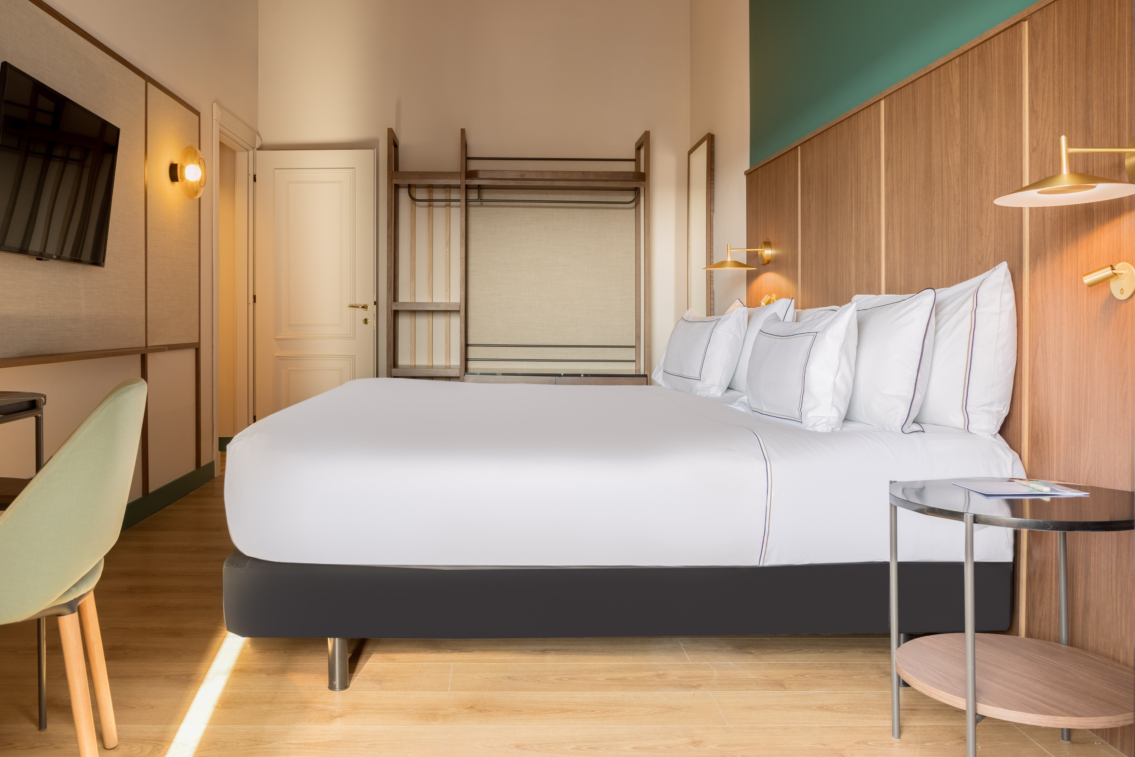 Modern hotel room with white bed, wooden details, and gold wall lamps.