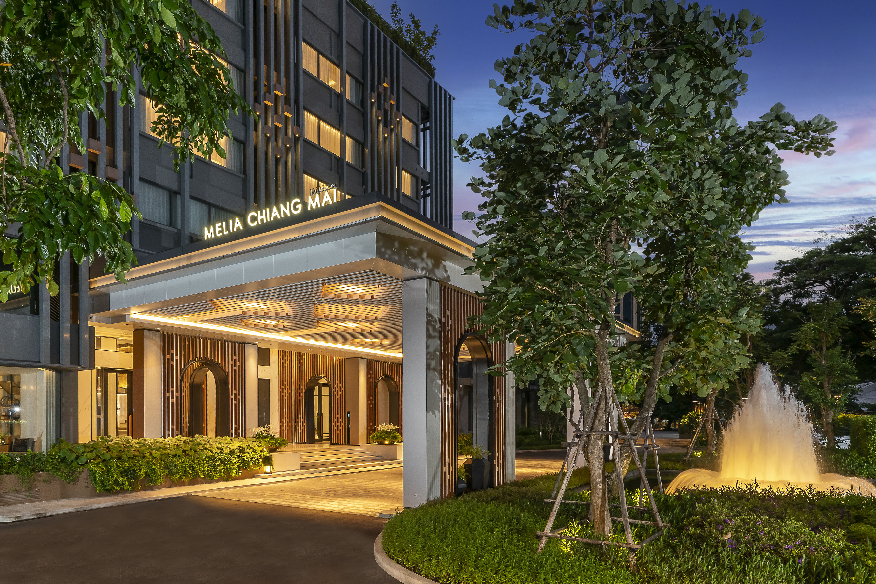 Melia Chiang Mai hotel entrance at dusk, illuminated, with fountain and trees.