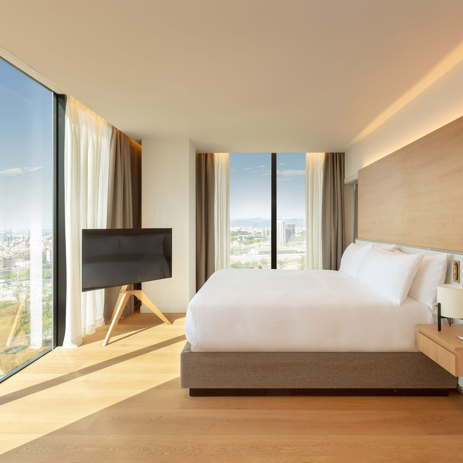 Habitación de hotel moderna con cama king, ventanales y vistas a la ciudad.