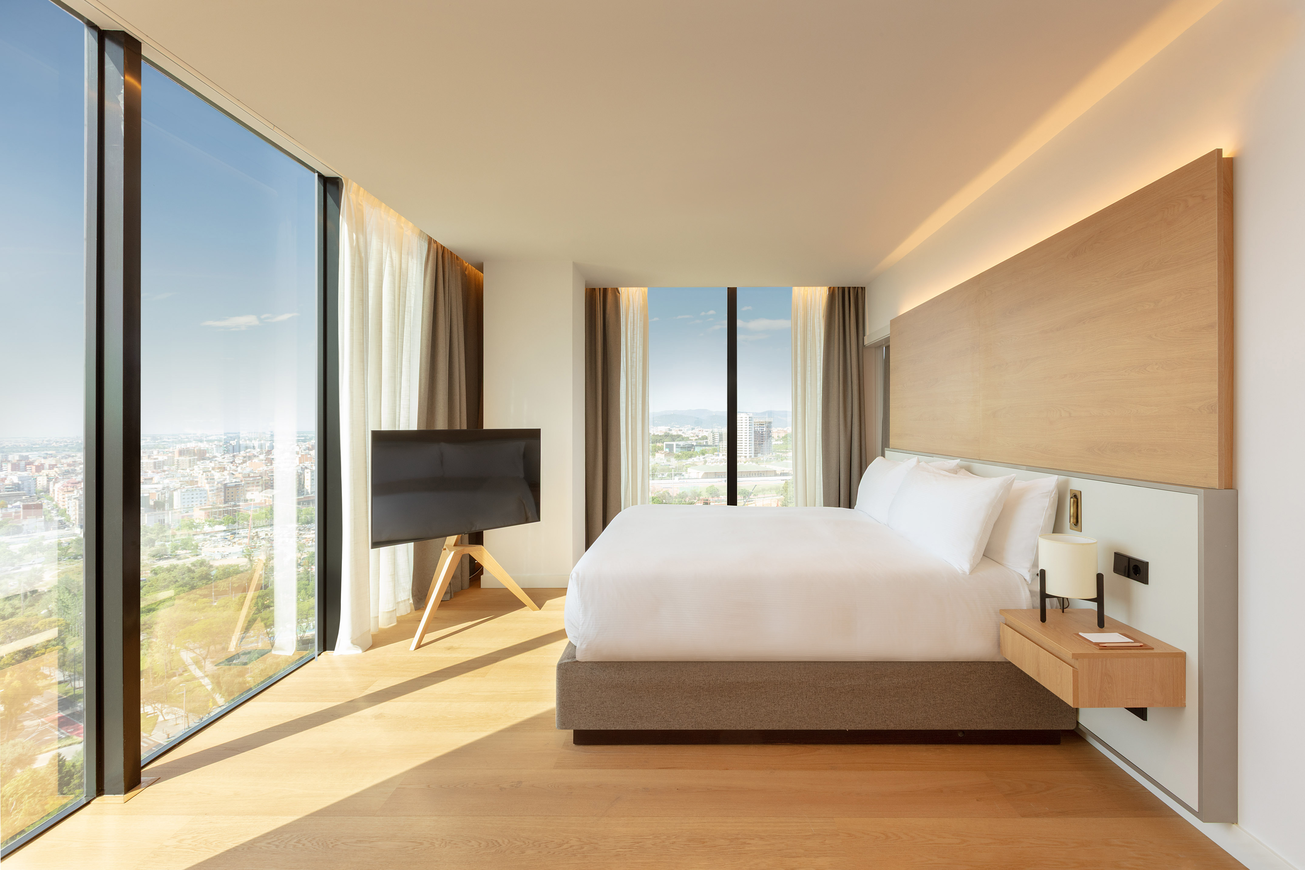 Habitación de hotel moderna con cama king, ventanales y vistas a la ciudad.