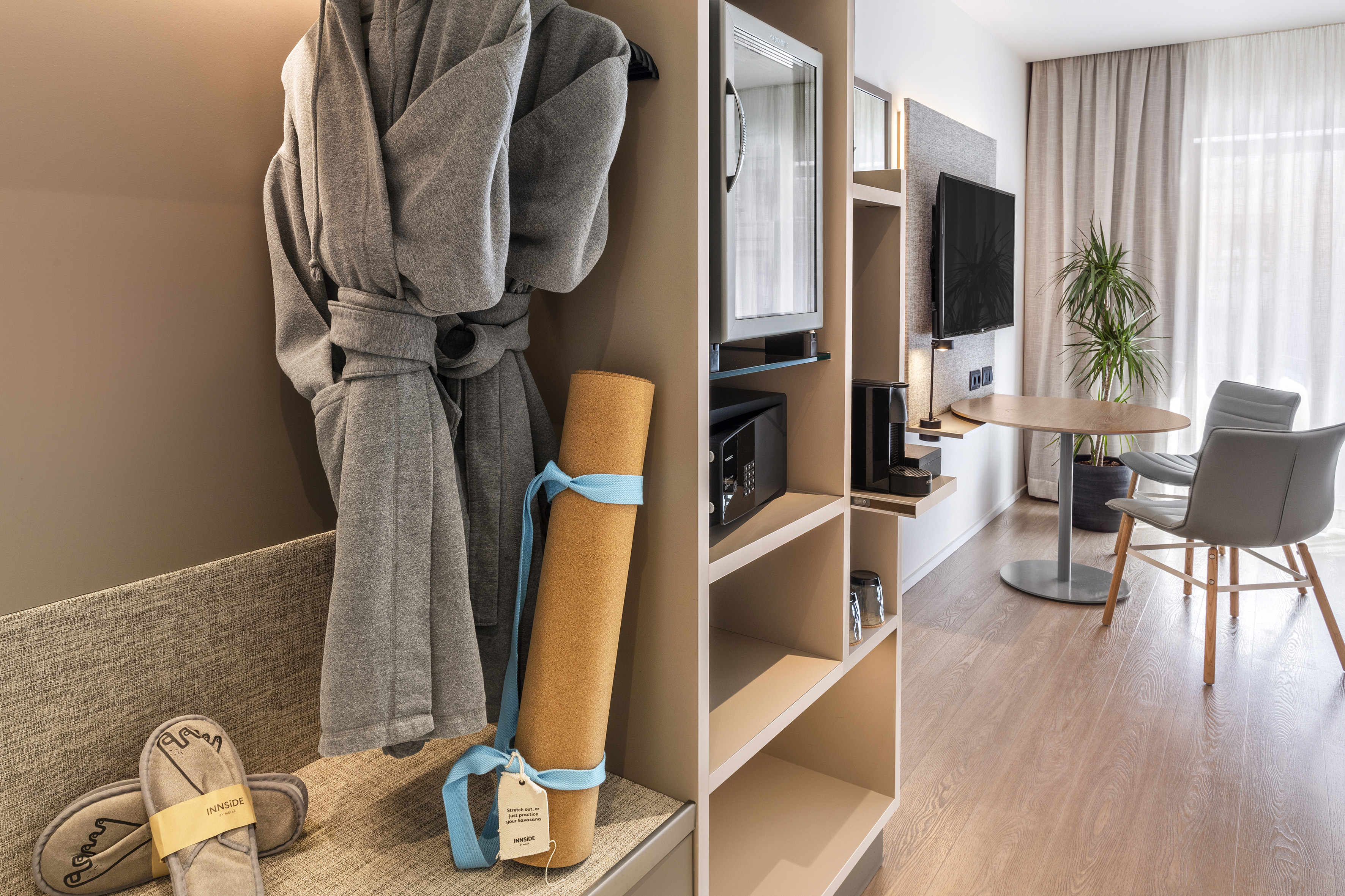 Hotel room with bathrobe, yoga mat, slippers, mini-bar, and dining area.
