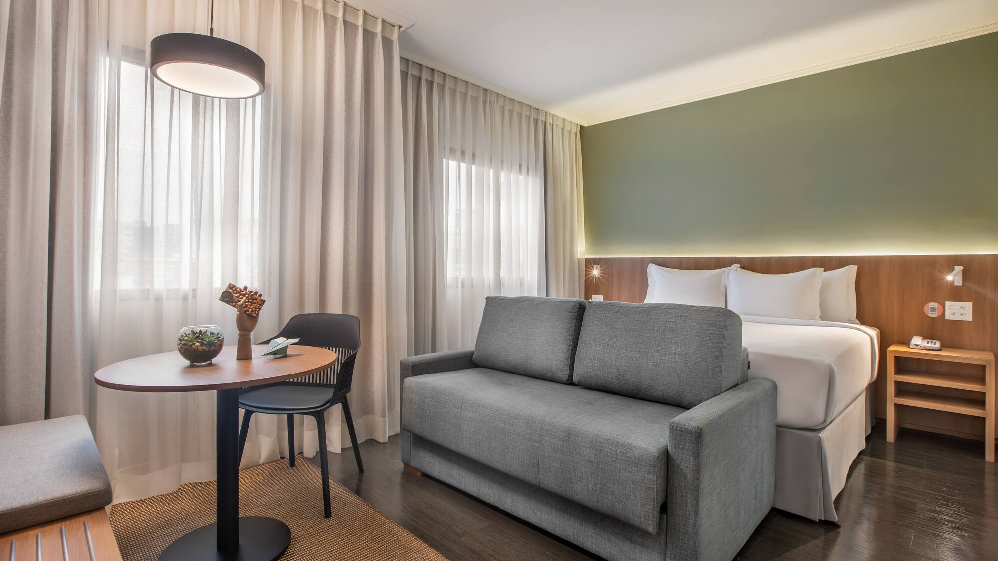 Modern hotel room with bed, gray sofa bed, and small table.