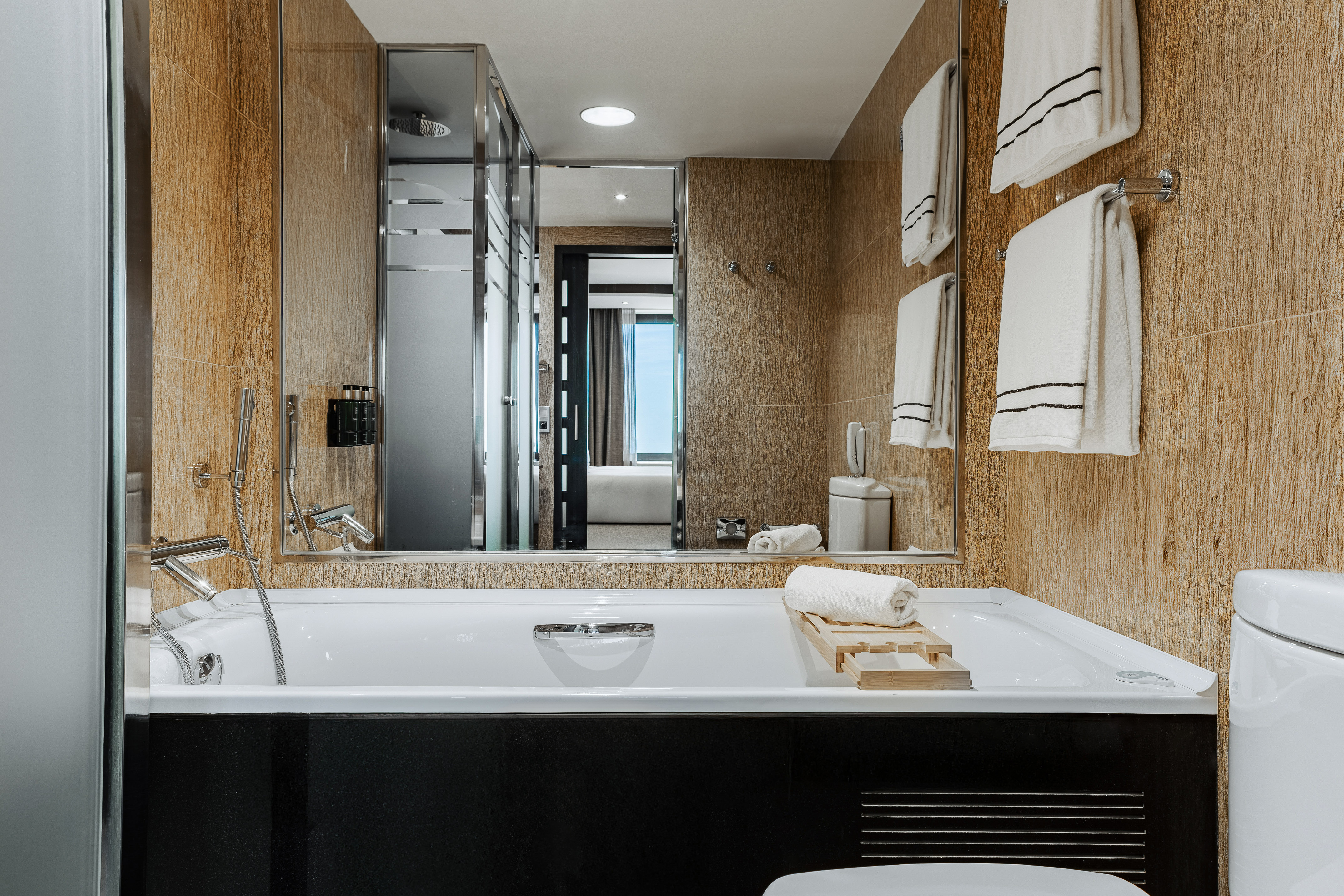 Modern bathroom with a white bathtub, brown tiled walls, white towels, and shower.