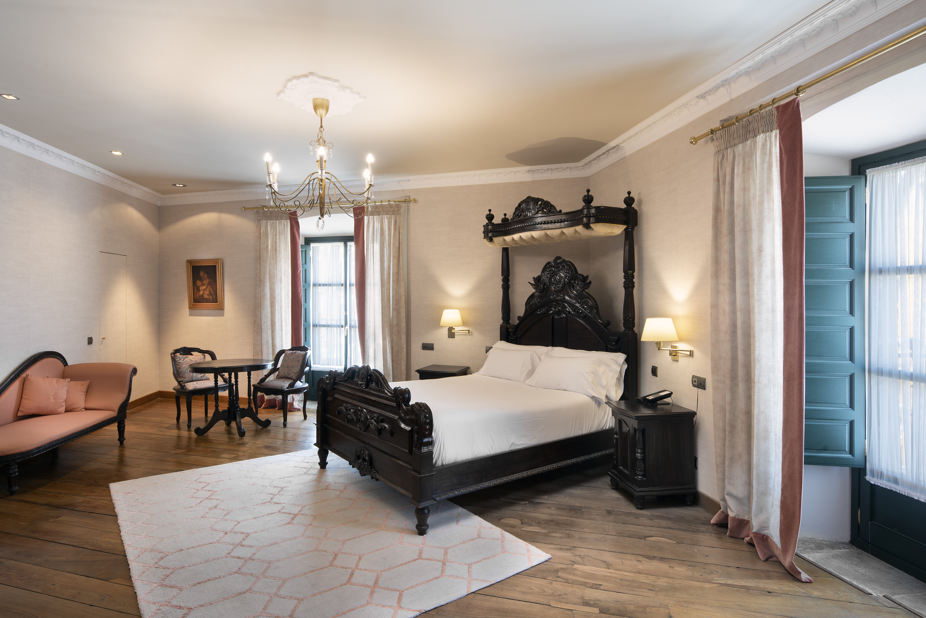 Elegant hotel room with carved four-poster bed, chandelier, and pink chaise lounge.