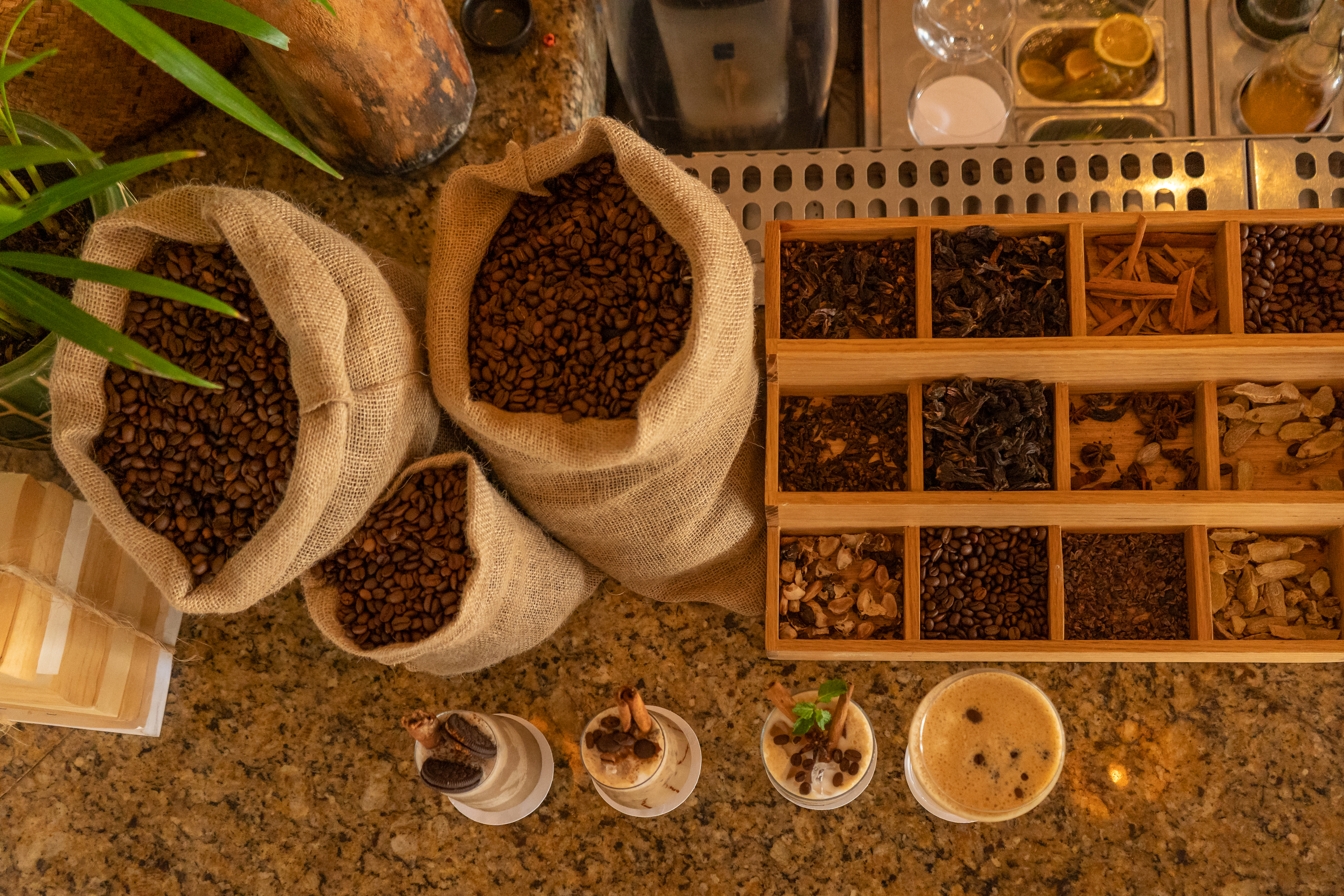 Roasted coffee beans in burlap sacks, spice tray, and four coffee drinks.