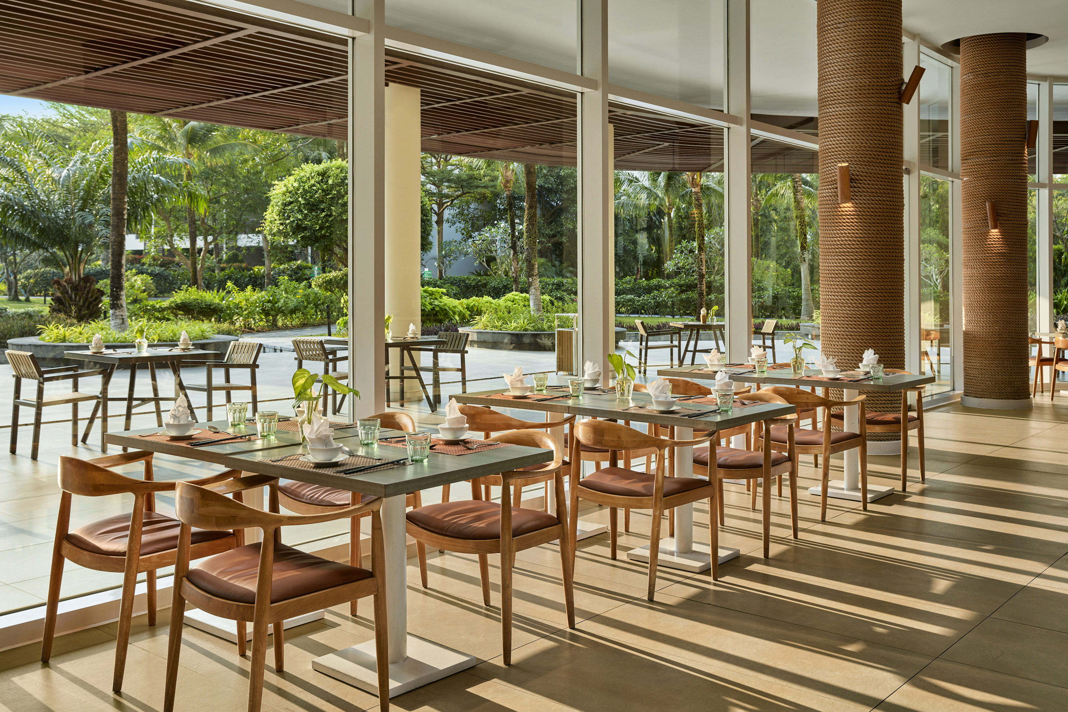 Restaurant dining area with set tables, tropical garden view, and modern decor.