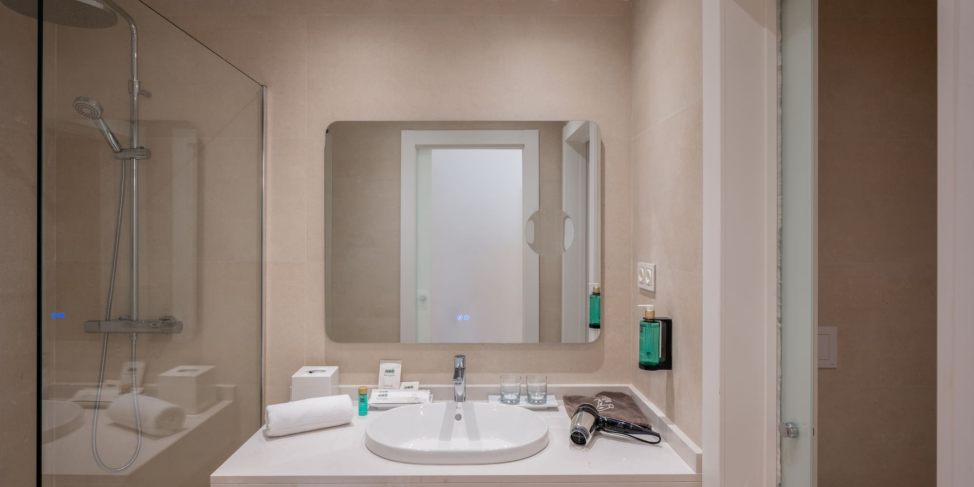 Modern hotel bathroom with walk-in shower, vanity sink, large mirror, and amenities.