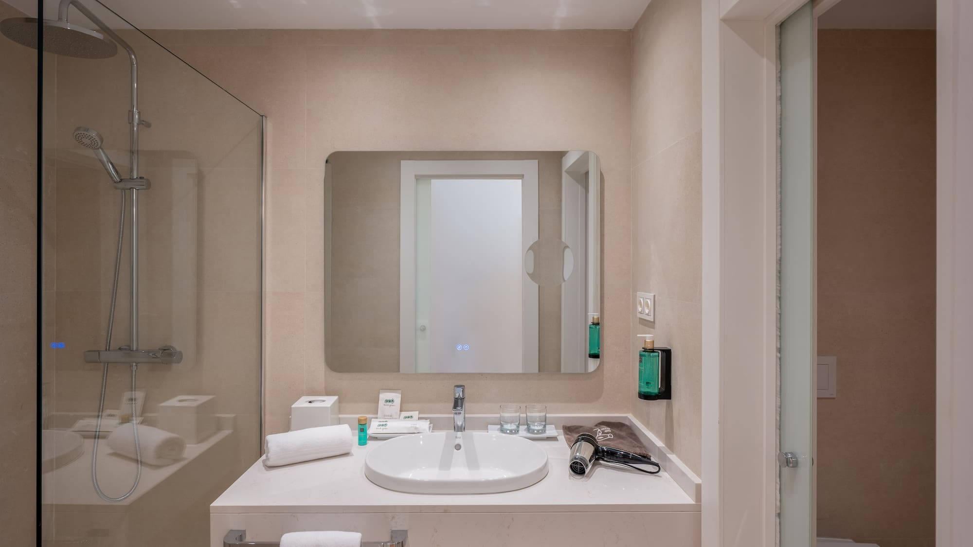 Modern hotel bathroom with walk-in shower, vanity sink, and large mirror.