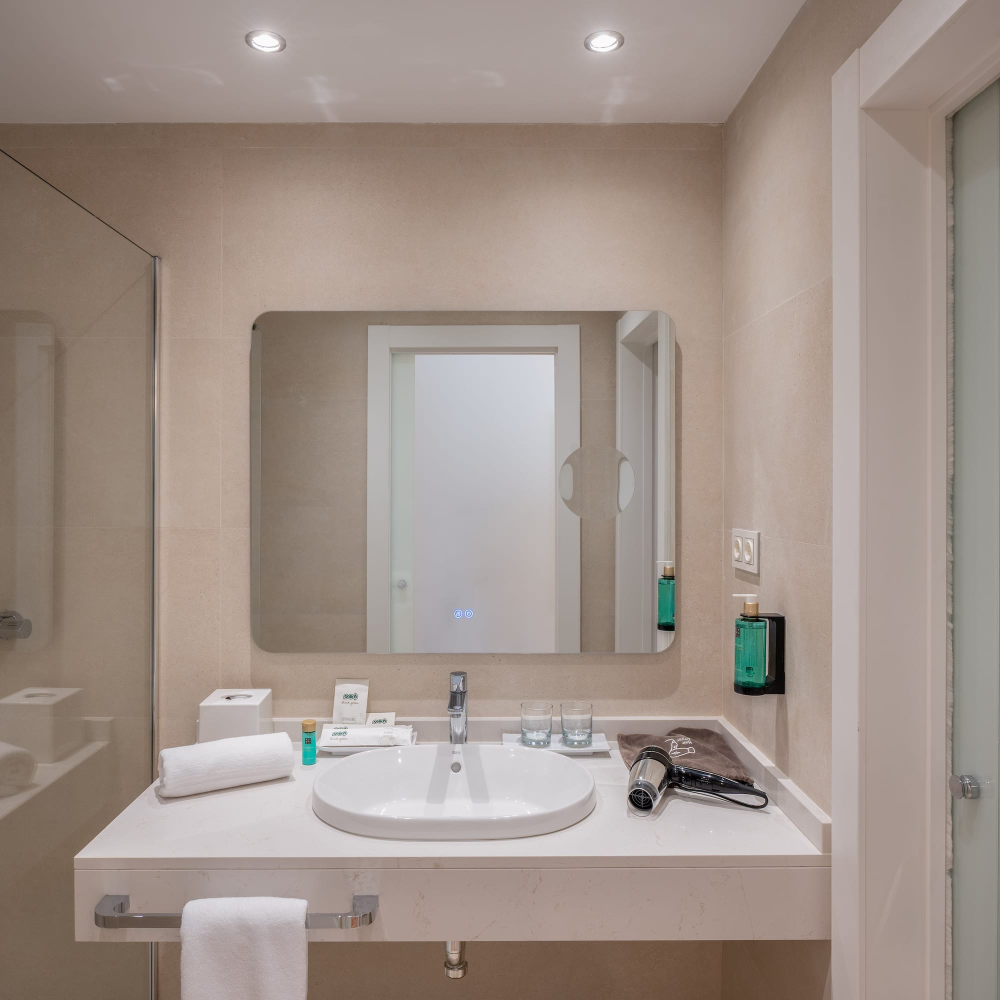 Modern hotel bathroom with walk-in shower, vanity sink, large mirror, and amenities.