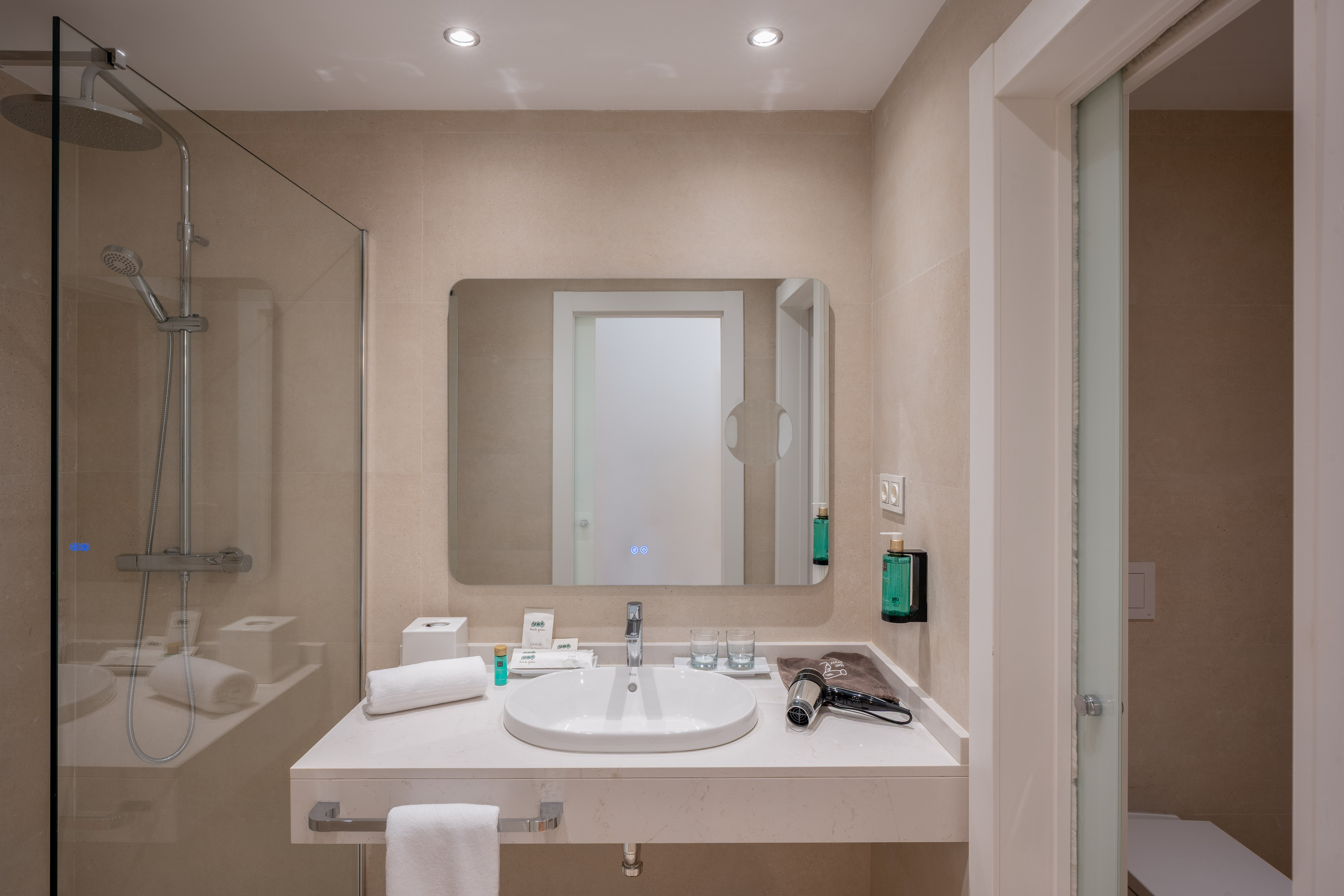 Modern hotel bathroom with walk-in shower, vanity sink, and large mirror.