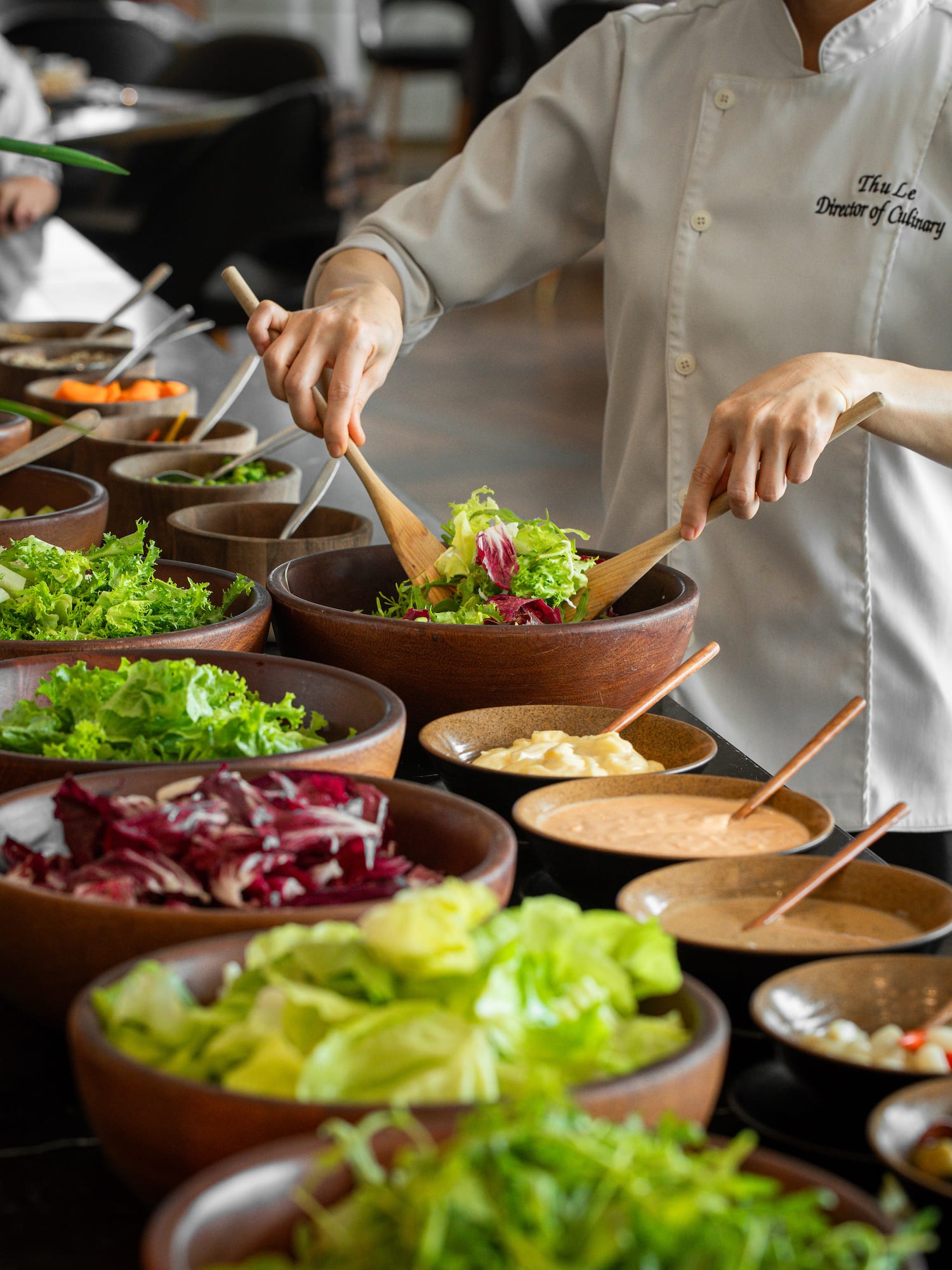 a person holding wooden spoons in a bowl of salad