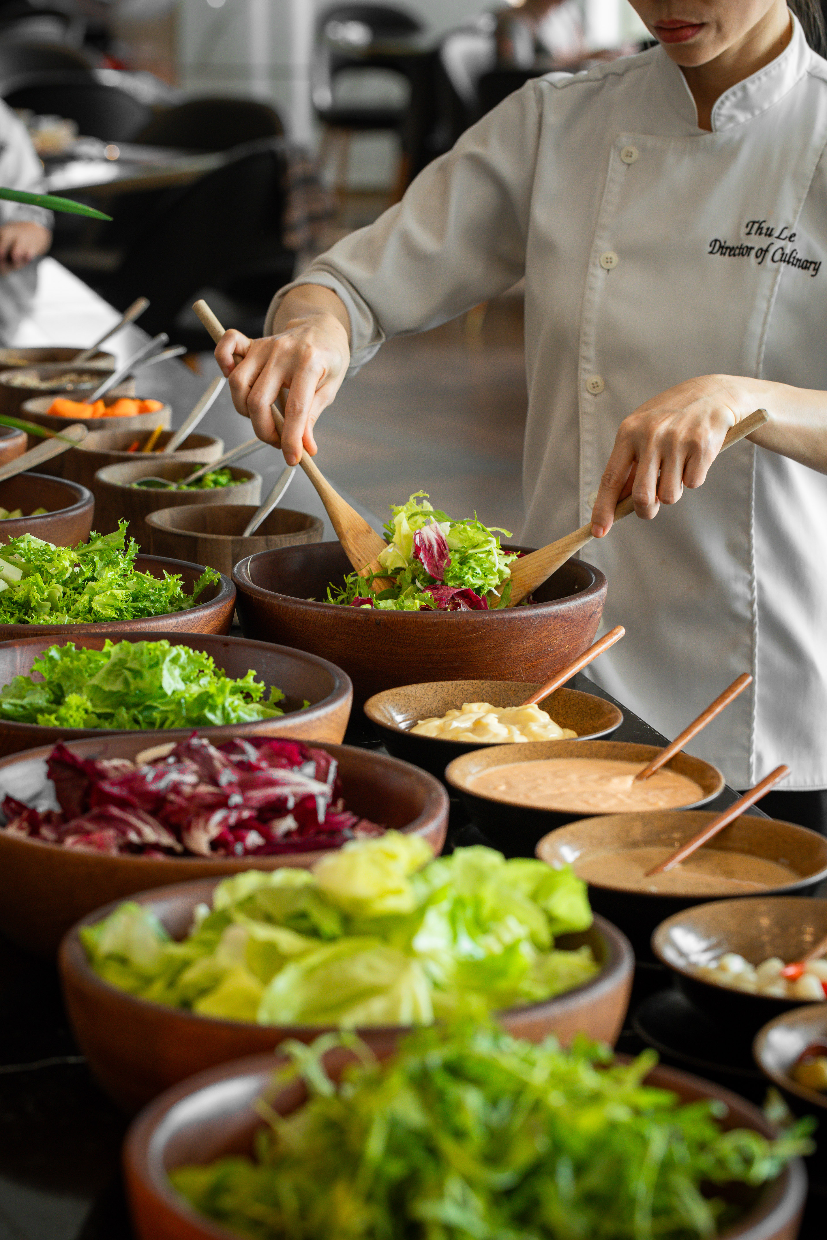 Chef Thu Le mixing fresh greens in a wooden bowl at a salad bar buffet.